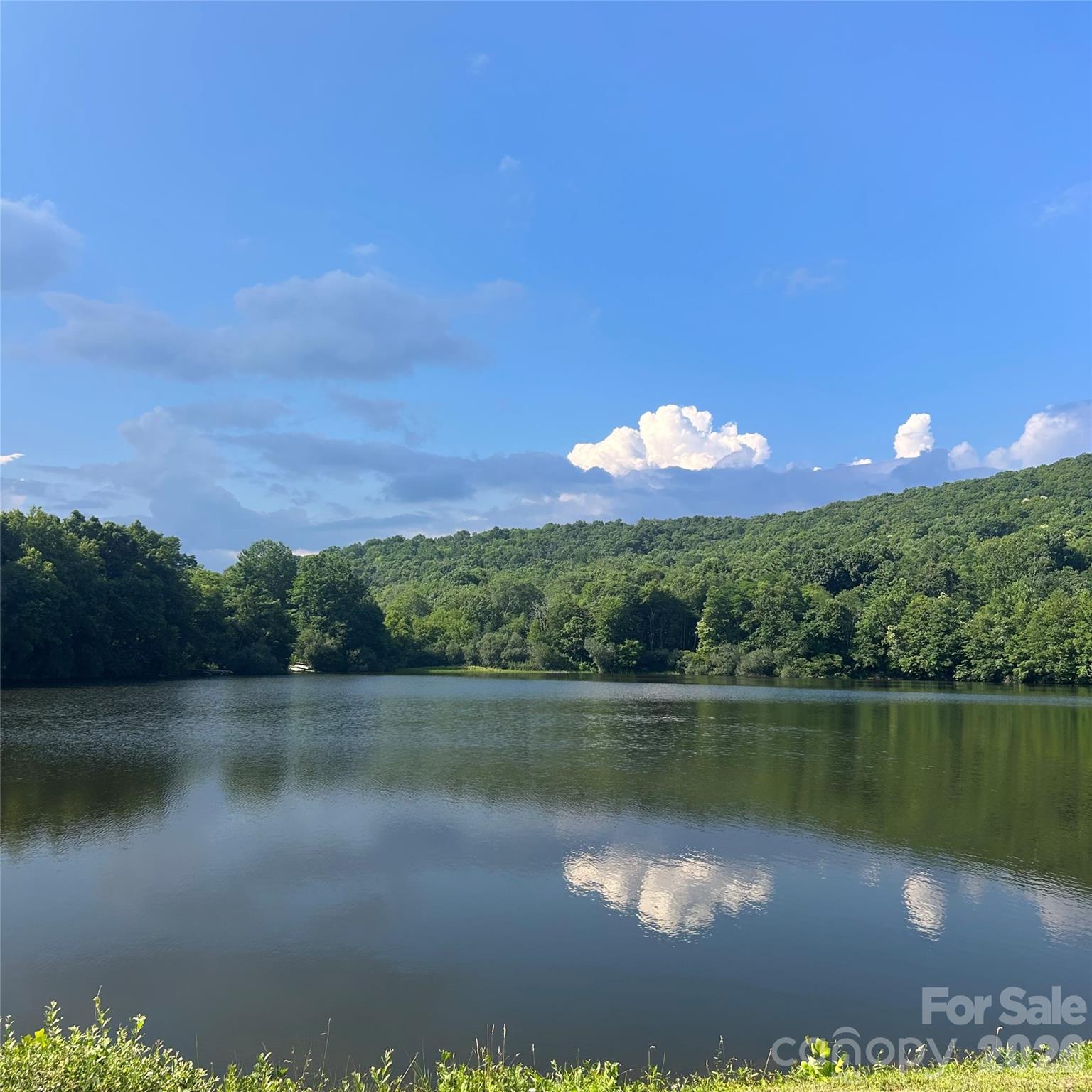 A beautiful Flat Top Mountain retreat with a 10 acre community spring-fed lake at 4000 feet elevation. There are over 250 acres of shared community green space with an abundance of walking trails and room for gatherings, volleyball, lake activities. The wooded areas around the home, ensure lasting privacy while maintaining a warm, community oriented atmosphere. A beautiful, pristine lake awaits-perfect for swimming, fishing, paddle boarding. Unwind with neighbors during casual summer evenings and gatherings at the dock, or retreat to your private covered porch or deck. Designed for both comfort and entertaining, the home features a large covered front porch with an expansive kitchen/dining area, open floor plan, vaulted ceilings with beams, a gorgeous gas stone fireplace on the main level and a wood-burning stove on the basement level. The primary suite includes French doors to the front deck ideal for waking to Birdsong and fresh mountain air. Basement area is fully finished and offers a guest room/office and a private gym space, along with a family room, and a workshop. A gorgeous, 10 minute drive up the mountain off of old Fort Road. Home also features a six person hot tub and a Kawasaki side-by-side mule for getting around the mountain trails to access the different mountain vistas within the community. Short term rentals are not allowed.