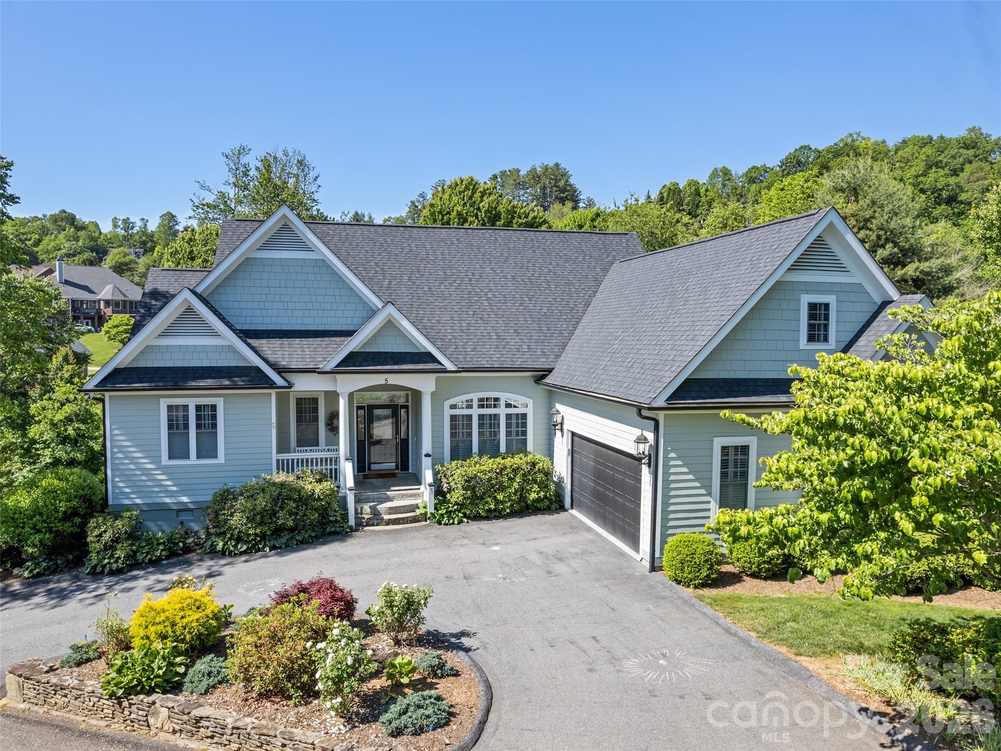 In the gated High Vista Falls community, this Arts and Crafts-style residence offers one-level living in a private cul-de-sac setting with peaceful wooded surroundings and a small creek bordering the backyard. On approximately 0.41 acres, the home features three bedrooms, two full baths and one half-bath with approximately 2,200 square feet of thoughtfully designed living space. Designed for comfort and functionality, the main-level floor plan includes the primary living areas and bedrooms, allowing for convenient everyday living. Updates include hardwood floors, an updated heating and air conditioning unit, updated dishwasher and cooktop, an electric fireplace and ADT security cameras, enhancing convenience and functionality throughout the home. New roof and exterior paint in 2022. Above the garage, a spacious bonus room provides flexibility for a media room, office, workout room, guest accommodations or hobby space. The home’s architectural character is complemented by a serene setting that offers privacy and a quiet mountain lifestyle. The living spaces are designed to accommodate gathering and entertaining while maintaining a warm, comfortable atmosphere. Natural surroundings and mature landscaping enhance the sense of retreat, with the sounds of the creek adding to the property’s tranquil environment. The cul-de-sac location further contributes to limited traffic and a more private residential experience. High Vista Falls is a gated mountain community known for its natural beauty and lifestyle amenities. Residents enjoy access to a community clubhouse, swimming pool, tennis courts, pickleball courts, neighborhood pub and recreational trails. Optional golf club membership opportunities are also available within the community. The neighborhood provides convenient access to Asheville Regional Airport, Hendersonville, Asheville dining and breweries, local shopping and outdoor recreation throughout Western North Carolina. Whether seeking a primary residence or mountain retreat, 5 Split Creek Court offers a combination of one-level living, flexible space, community amenities and a peaceful setting within one of Mills River’s established gated communities.