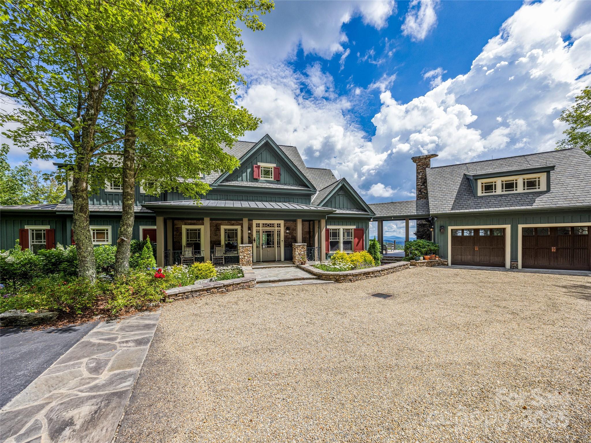 Best Mountain Views in Lake Toxaway! Experience refined mountain living on three outstanding Meadow Ridge lots spanning over 7 private acres with panoramic views of Cold Mountain, Panthertail Mountain, and the Blue Ridge Parkway. This exceptional 5-bed, 7-bath estate blends luxury and comfort with vaulted ceilings, custom woodwork, and three impressive native stone fireplaces. The main house features a spacious eat-in kitchen with granite countertops and limestone floors, antique heart of pine floors, along with a fitness room and multiple living spaces designed for relaxation and entertaining, all with stunning views.
Outdoor living shines with two entertainment terraces, an open area for seating around a native stone fireplace with sweeping mountain views, a covered passage between main home and garage/guest quarters, and professionally landscaped grounds complete with a stream and waterfall. The separate light-filled guest quarters above the garage includes a full bath and kitchenette, and large windows with breathtaking views—perfect for hosting visitors. Modern conveniences include reliable Starlink internet that is connected to the whole-home generator, ensuring comfort and connectivity in every season.
Every detail has been carefully considered to create a peaceful, elegant retreat. Offered fully furnished with some exceptions, this home is the pinnacle of fine mountain living.