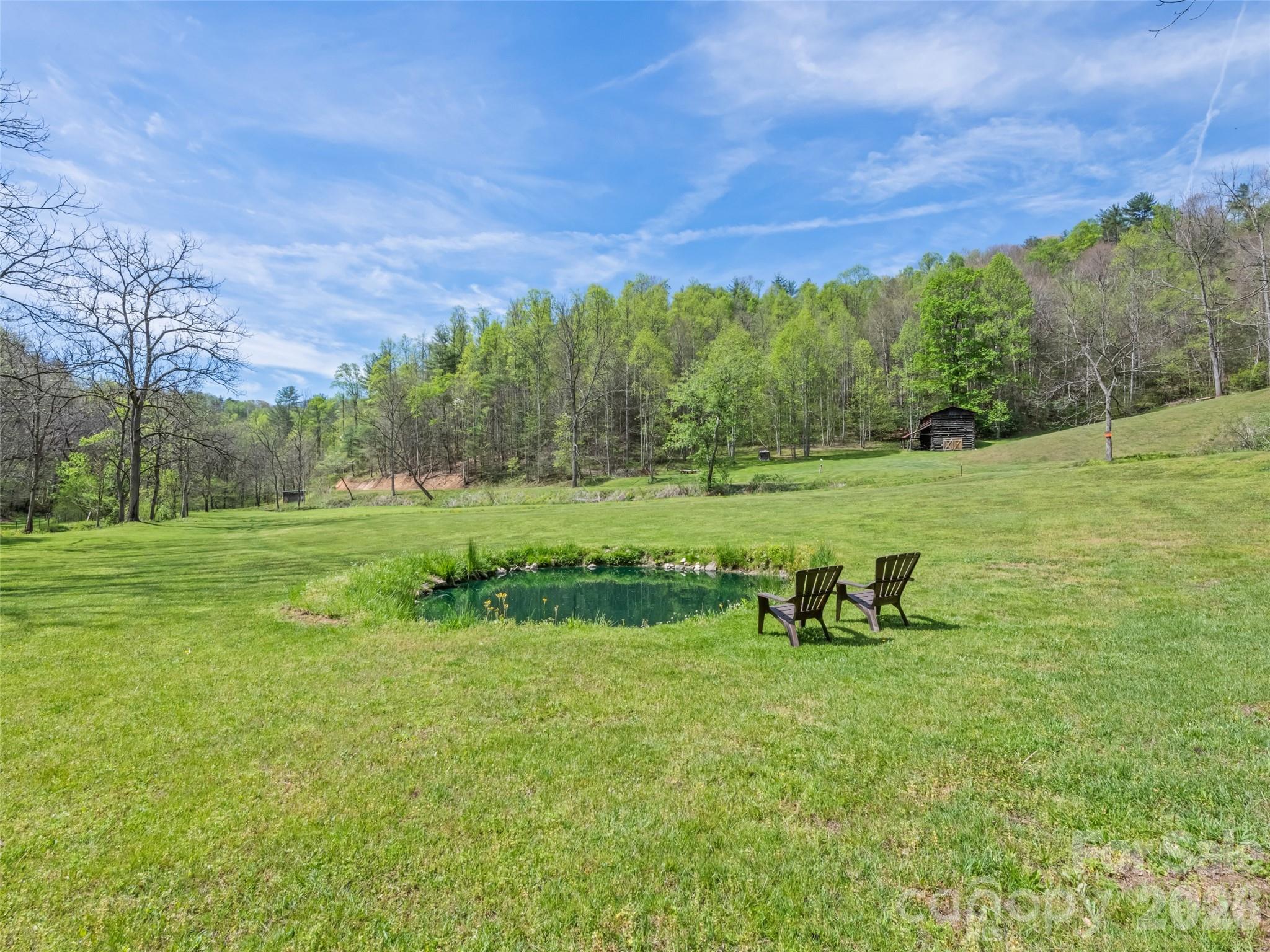 Set on 47± acres of rolling mountain beauty, this rare Fines Creek retreat invites you to slow down and live immersed in nature—while offering exceptional potential as a private estate. The mix of open pasture, gentle terrain, and existing roadbeds creates an ideal foundation for riding trails, and future barn expansion. The historic 1890 “Hugh Rogers” cabin offers 3 bedrooms and 1 bath, where a welcoming covered front porch and a living room fireplace crafted from native creek stone create a warm, timeless gathering space. A classic farmhouse kitchen completes the rustic charm. Step outside and the lifestyle unfolds—ride across open fields, explore wooded trails, cast a line in two stocked ponds, or listen to the creek as it winds through the property. With ample water sources and usable land, the property is well-suited for horses or a small-scale farm operation. Additional structures enhance the experience, including a character-filled gentleman’s cabin with a loft bunk room, a unique bath featuring a water trough tub/shower, and "The Snug Cottage," offering additional guest quarters. A tobacco barn, equipment barn, RV setup, and storage buildings provide flexibility for equestrian use, storage, or conversion to stables. With multiple building sites, established infrastructure, and expansive usable acreage, the possibilities are wide-ranging—from an estate or family compound to an event venue or outdoor retreat. Unrestricted and conveniently located near I-40, you’ll enjoy easy access to Asheville or Tennessee while feeling worlds away. This is more than property—it’s a place to create a legacy, embrace the outdoors, and experience mountain living at its finest.