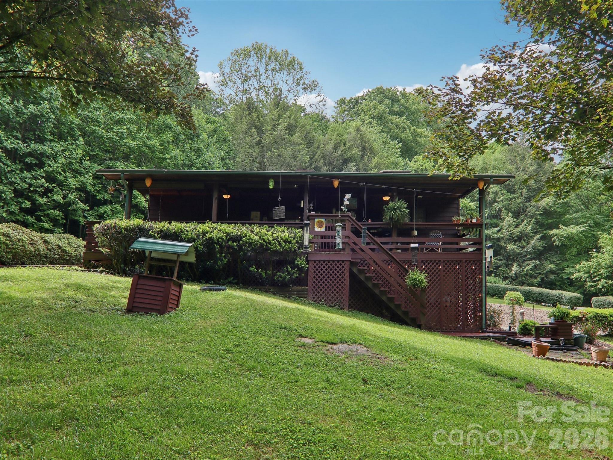 Experience mountain serenity in this inviting 3-bedroom, 3-bath home nestled on a peaceful, partially wooded lot. Surrounded by mature trees, a flat yard, and multiple water features, this tranquil retreat is perfect for nature lovers seeking both privacy and convenience. Two driveways and a two-car garage provide ample parking, including main-level access for easy entry, while the covered front porch invites you to relax and enjoy the crisp mountain air. Inside, the living room features a vaulted ceiling and flows into a well-appointed kitchen with appliances updated in 2022. Laundry hookups on both the main and basement levels make for true one-level living if desired. The finished basement, complete with a full bath and access from both the main floor and garage, offers excellent guest or rental potential. Conveniently located near Maggie Valley, Waynesville, and I-40, this property perfectly blends comfort, function, and location—ideal as a full-time residence, weekend escape, or investment opportunity.