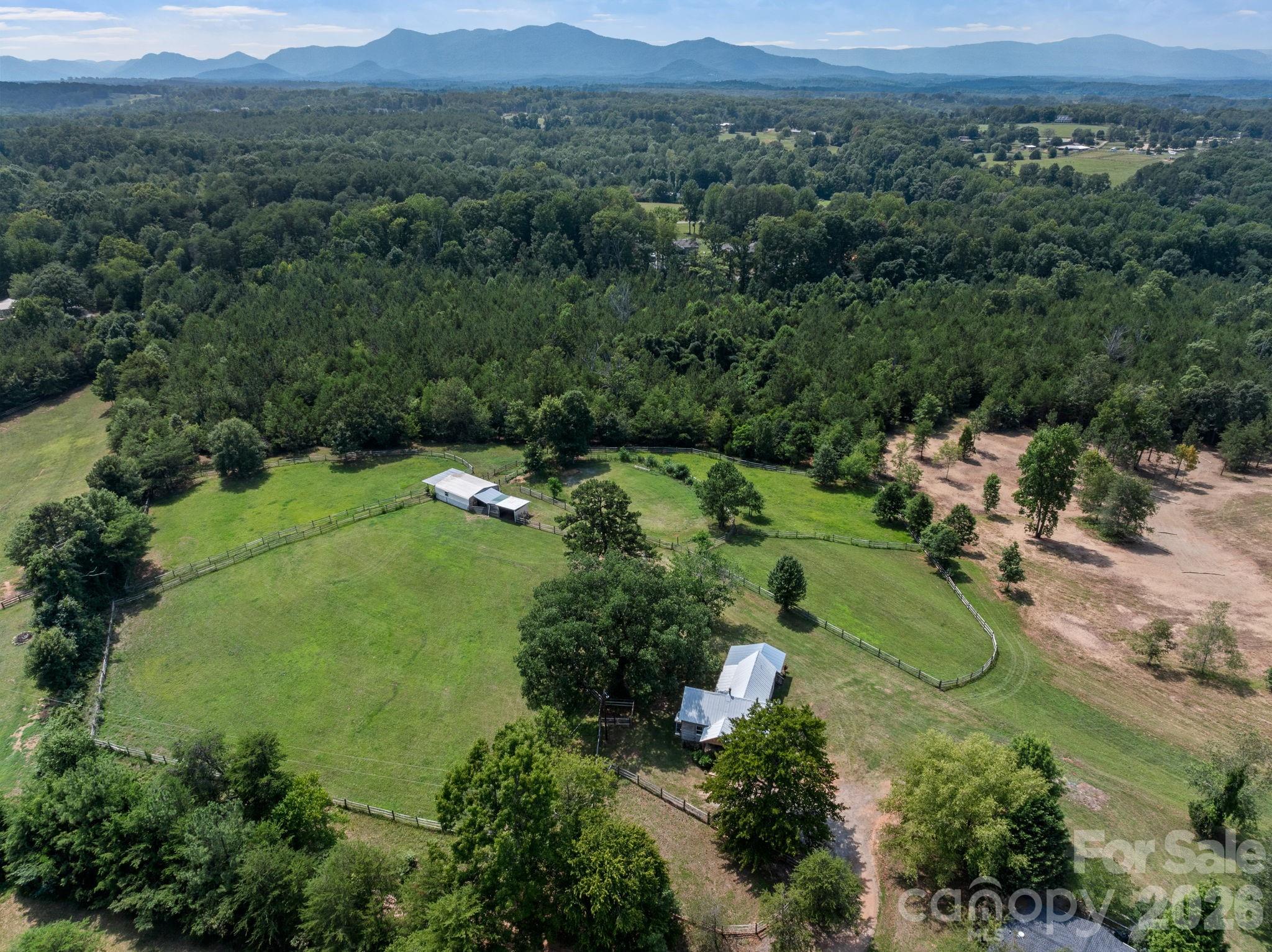 Over 11 acres of Tryon horse country, just minutes from Tryon International Equestrian Center, with long-range mountain views that stop you in your tracks. 3 stall barn, run-in shed, split rail fenced pasture, open meadow, and mature hardwoods make this a great fit for horses, a weekend getaway, or a full-time retreat in a setting that's hard to find this close to TIEC. The 1-bedroom, 1-bath cottage (857 sq ft, ~1,311 sq ft including covered porch, patio, and deck) offers an eat-in kitchen open to a vaulted living room, an full bath, and a large dedicated closet/laundry room, a front porch and a covered deck built for taking in the view. The cottage is sold as-is and best suited to a buyer who sees the bones and character. Potential to also purchase an adjacent ~3.5-acre lot with a 3 bedroom and 2 bath manufactured home.