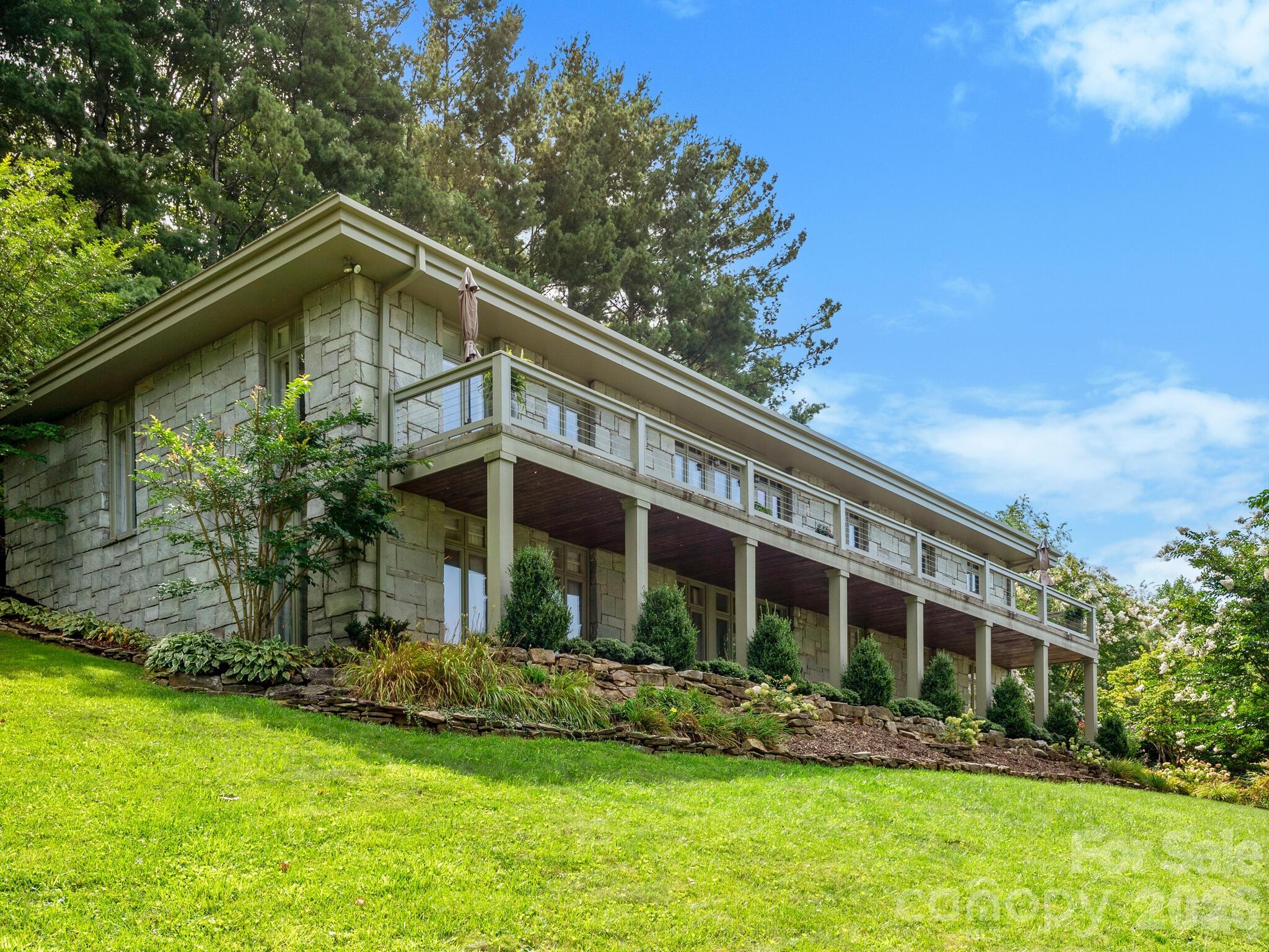 Located on the slopes of Sunset Mountain, 65 Crestwood Road is a rare legacy estate that captures the timeless elegance, architectural integrity, and gracious living that define Asheville’s most treasured homes. Originally constructed by Abbott Construction for the Pearlman family, this exceptional four-bedroom, three-and-a-half-bath residence was thoughtfully designed to embrace both the beauty of the land and the rhythm of everyday living.
Approached by a long private drive, the home welcomes guests beneath a stately porte-cochère and into interiors filled with warmth, craftsmanship, and extraordinary natural light. Built with enduring Grandfather Mountain stone from Linville, North Carolina, the residence showcases original hardwood floors, custom wood detailing, expansive windows, dome-shaped skylights, and beautifully proportioned living spaces designed to bring the outdoors in.

Positioned to maximize sweeping mountain ridges and sparkling city views, every room opens to the beauty of Asheville’s landscape. Expansive porches and terraces create seamless indoor-outdoor living, offering unforgettable spaces for entertaining, quiet evenings, and year-round enjoyment of sunsets over the city.

The main-level primary suite is a private retreat with breathtaking views and direct access to the surrounding outdoor spaces. The lower level offers three additional bedrooms, beautifully connected sitting areas, and walkout access to established perennial gardens, walking paths, and peaceful outdoor living spaces carefully designed to complement the natural setting.

Meticulously maintained with no deferred maintenance, this home offers a rare combination of timeless architecture, exceptional craftsmanship, and modern livability. Located just minutes from downtown Asheville, yet privately positioned within one of the city’s most cherished walking neighborhoods without restrictive HOA oversight, 65 Crestwood Road represents a remarkable opportunity to own a true Sunset Mountain legacy property.

4 Bedrooms | 3.5 Bathrooms | Expansive Porches | Mountain & City Views | Minutes to Downtown Asheville | Legacy Property on Sunset Mountain
