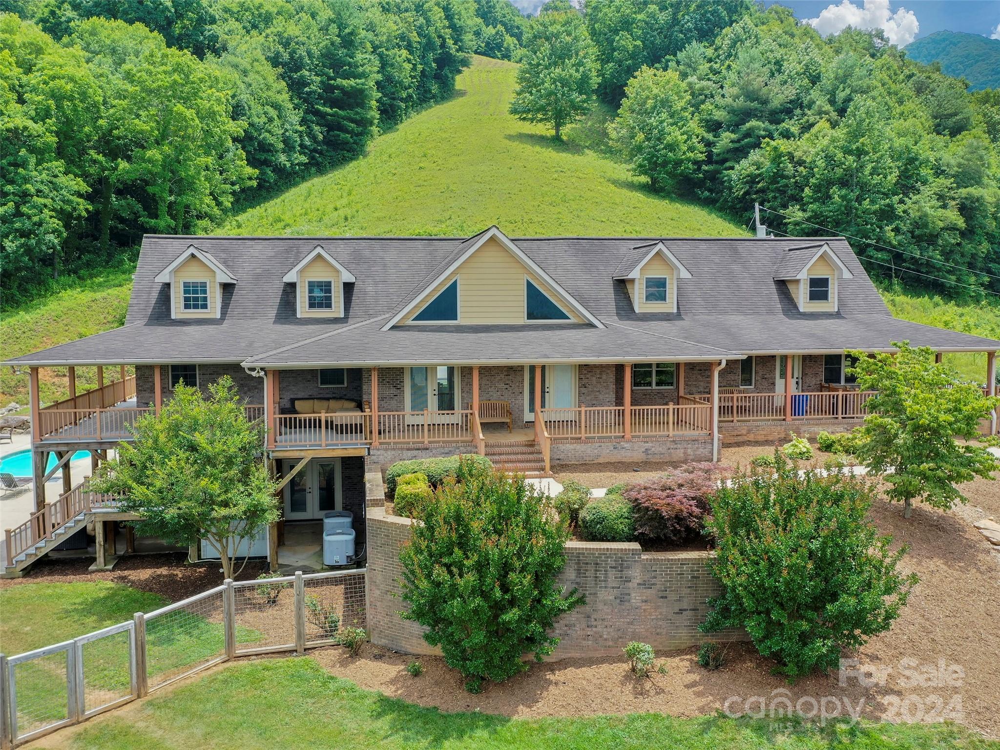 Atop 56+ picturesque acres in Fines Creek, this expansive estate offers unparalleled amenities. Boasting long-range views, an in-ground saltwater pool w/a cascading waterfall, an outdoor firepit, fenced pastures,  a 3-bay detached garage w/a tractor shed, & private trails leading to a nearby creek, the property truly has it all. The traditional brick home was vastly expanded in 2007, featuring a grand foyer, a 2-story great room w/vaulted ceilings & a beautiful fireplace, a primary suite w/a gas fireplace, a bay window, a granite double vanity, a jetted tub, & a large walk-in shower, as well as 2 large BR suites on the upper level & an updated laundry room. The original section boasts 1 BR/1 bath on the main level, + a bonus room & bath upstairs, a dining room w/vaulted ceilings, a loft, and a kitchen equipped w/granite countertops, like-new appliances, a wine cooler, and a walk-in pantry. The fully-finished basement w/a full bath and a rec room flows effortlessly out to the pool deck.