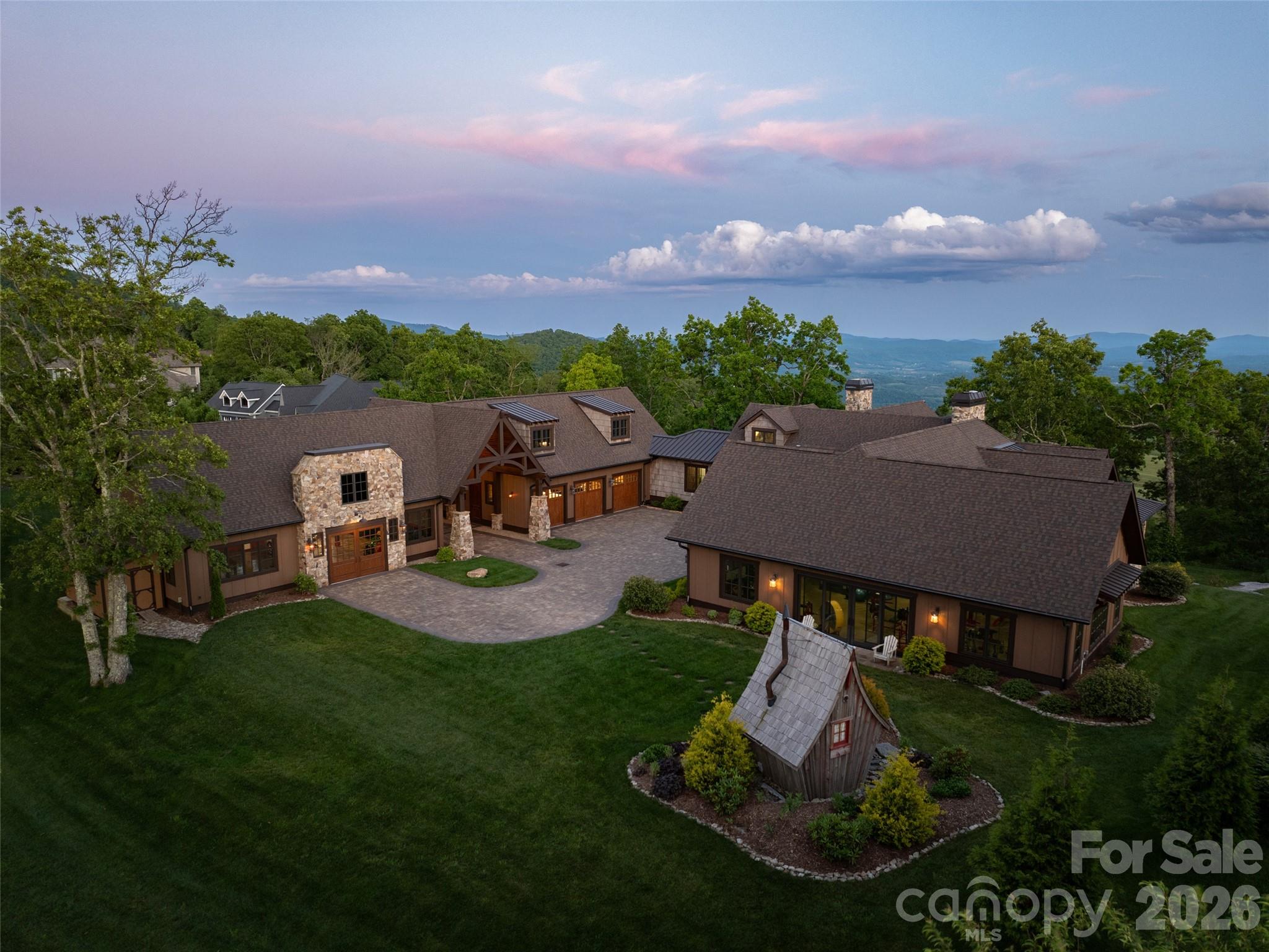 Perched at a commanding 3,800-foot elevation, this 5 BR / 5 BA architectural jewel is a rare, multi-generational legacy estate where modern luxury meets the enduring spirit of the mountains. Built in 2019, this custom post-and-beam timber frame home is a sophisticated sanctuary crafted to host today’s milestones and anchor a family's heritage for generations to come. Exceptionally rare, this showpiece is situated on 2.79 acres of meticulously manicured, usable mountain top space level enough to provide a secure canvas for play, pets to roam and an easy backdrop for alfresco entertaining. From its high-altitude vantage point, the estate captures breathtaking, multi-layered mountain panoramas from nearly every vantage point, while soaring glass doors effortlessly dissolve the boundaries between the refined interiors and the natural world. The interior narrative centers around a resplendent great room, where dramatic vaulted ceilings and rustic reclaimed timber elements frame a monumental, two-story hand-stacked stone fireplace. Both commanding and grounded, this central space transitions seamlessly into the epicurean kitchen—a culinary tour de force featuring custom cabinetry, a professional-grade Thermador appliance suite with a six-burner gas range, double wall ovens and a sprawling backlit onyx island with seating for 6.   A dedicated wellness wing, also on the main level, features a high-performance fitness studio that opens directly to the verdant lawns and a freestanding, custom-designed Nordic sauna house. The attached oversized three-car garage highlights loads of room for storage within and above the parking area as well as a separate workshop / craft room. A detached six-car collector's garage offers a versatile footprint that could be easily transformed into a private guest cottage, game lounge or media space...endless options.  With long term accessibility in mind, this  signature estate was intentionally curated to elegantly bridge the gap between effortless daily utility and artisanal lifestyle nuances without compromising its organic, unpretentious elegance.  This is a true mountain sanctuary that beckons real life and sensory rich memories to be made throughout generations.