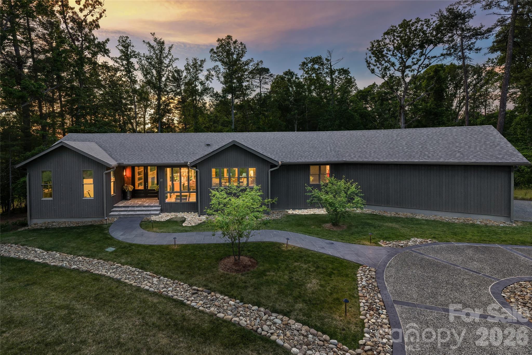 This award-winning Weaverville residence offers a refined take on modern mountain living, blending striking architecture with warm organic materials and thoughtfully curated design. Recognized in the 2024 Parade of Homes, the home showcases exceptional craftsmanship and elevated finishes throughout, creating a retreat that feels sophisticated and deeply livable. Wrapped in Nakamoto Forestry Shou Sugi Ban Japanese cypress siding finished in a rich gray stain, the exterior makes a bold architectural statement while harmonizing beautifully with the surrounding landscape. Hickory wood floors run throughout the home, grounding the contemporary interiors with warmth and texture. Inside, expansive living spaces are layered with custom details including Phillip Jeffries and Schumacher wall coverings, designer lighting, bespoke cabinetry, and carefully selected natural stone finishes that bring depth and character to every room. At the heart of the home, the kitchen seamlessly blends form and function with ebony and cherry cabinetry, dramatic Belvedere granite countertops, and a custom powder-coated range hood in a muted green hue. Open-concept living and dining areas are designed for effortless entertaining, anchored by a marble mosaic fireplace and expansive windows that frame the wooded mountain setting. The primary suite offers a spa-inspired retreat with terrazzo tile, a luxurious steam shower and serene layered textures that create a calming atmosphere. Outdoor living was equally prioritized, featuring Trex decking, Peacock pavers, professional landscape lighting, and beautifully maintained grounds supported by a full front and backyard sprinkler system. Additional features include an oversized garage with epoxy flooring and a whole-house generator, providing exceptional convenience, comfort and peace of mind. Blending modern design, elevated finishes and functional luxury, this remarkable home delivers an exceptional standard of mountain living in one of Western North Carolina’s desirable settings.