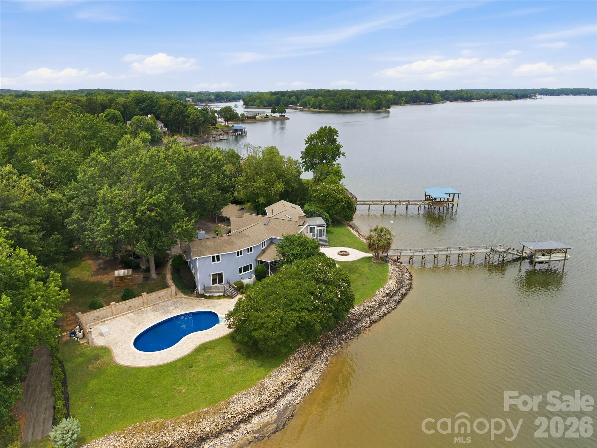 Discover the joy of lakefront living with breathtaking long-range views of Lake Wylie from nearly every room in this remarkable waterfront retreat. The versatile floorplan is tailored to accommodate a variety of lifestyles and uses, offering the perfect blend of comfortable everyday living, entertaining spaces, private retreats, and opportunities for a home office, guest accommodations, or hobby areas. Expansive windows capture the stunning scenery, bringing the beauty of the outdoors inside while creating a warm and inviting atmosphere throughout.  The gourmet kitchen features stainless steel appliances, a gas cooktop, Bosch dishwasher, granite countertops, and a stunning wood ceiling. Designed for entertaining, the family room flows seamlessly into a spacious recreation room and sunroom with heated floors.  The dramatic two-story dining room showcases vaulted wood ceilings and a fireplace providing space for both elegant gatherings and casual meals. The lake facing great room with fireplace, full bath, 2nd laundry area, and spacious 1st floor bedroom are perfect for a second owners suite or private guest wing. Upstairs, you'll find two generously sized secondary bedrooms and an impressive primary suite, complete with a spa-inspired bath featuring a tile shower, jetted tub, double vanity, and a private oversized terrace overlooking the lake. Outdoor living is unmatched with a massive Trex deck, 2 covered porches, a swimming pool, expansive paver patio, and fire pit area perfect for relaxed evenings. Boating enthusiasts will appreciate the covered deep water dock with lift and swimming platform, offering easy access to endless days on the water. With spectacular views, a highly desirable level waterfront lot, and a layout designed to adapt to your needs, this home offers both functionality and the serenity of a remarkable lakefront setting.
