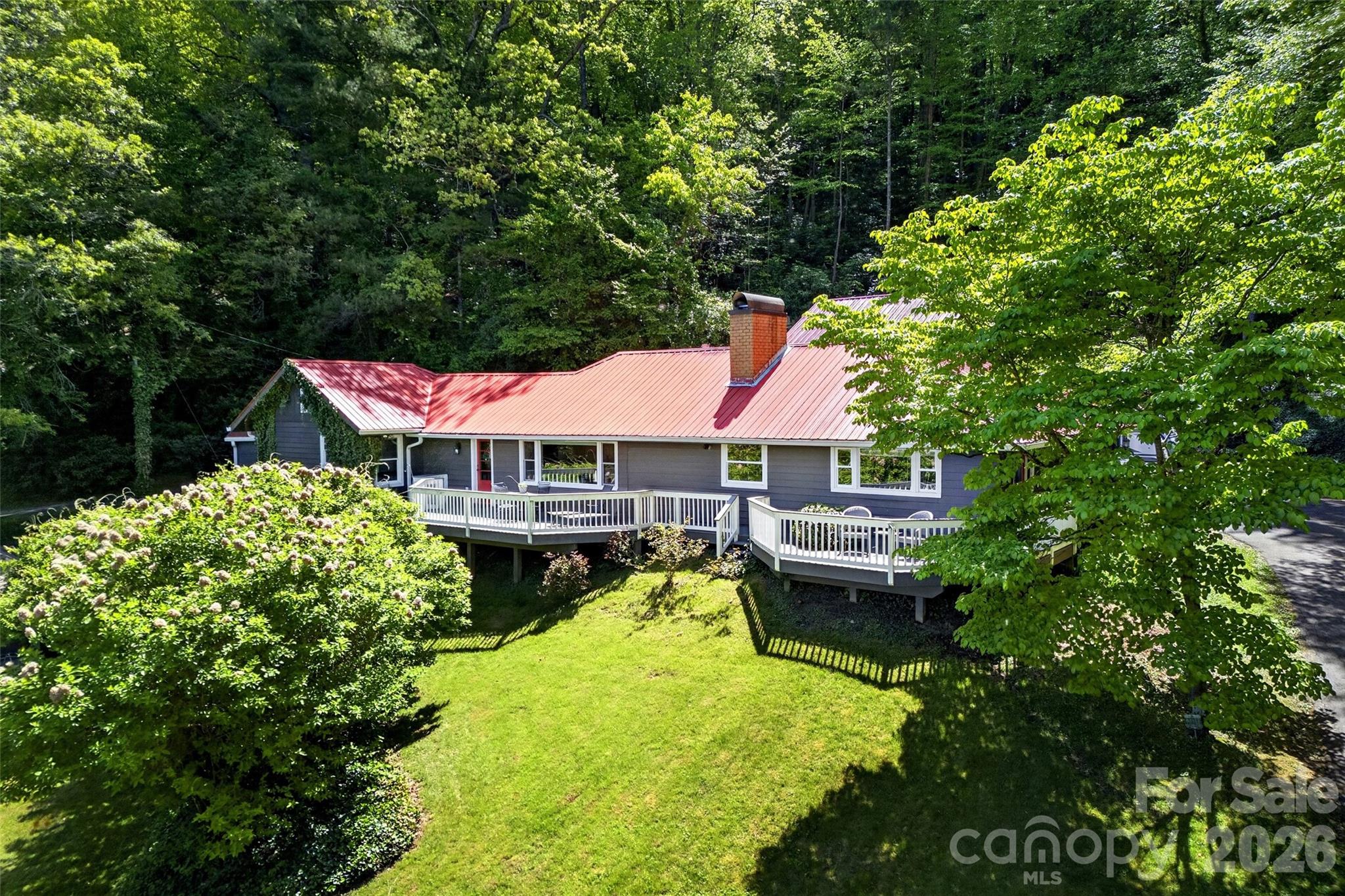 Some homes are special—you know it the moment you walk through the door. This is one of those homes.

Mountain views, timeless charm, and thoughtful design come together at 75 Old Lakey Gap Road in the heart of Black Mountain. Perched gently on a hill, this 4-bedroom, 3-bath home captures sweeping views of the Craggy Mountains and beyond, offering a peaceful retreat just minutes from town.

From the moment you arrive via the circular driveway, the striking red roof and welcoming red doors set the tone—inviting, distinctive, and full of character. Inside, the dining room features a beautiful brick floor, adding warmth and architectural interest that carries throughout the home. The inviting living area centers around a large fireplace and a stunning picture window that frames the mountain views—filling the space with natural light and bringing the outdoors in.

Designed for easy one-level living, the main floor includes a spacious primary suite with direct access to the deck—an ideal spot to enjoy morning coffee while taking in the mountain views and blooming hydrangeas. A cozy loft offers a flexible retreat for rainy afternoons, reading, or additional sleeping space.

The home also offers excellent guest accommodations, with a separate living area that can function as a private suite—complete with bedroom, bath, and lounge space.

A durable metal roof provides peace of mind, while the expansive deck creates seamless indoor-outdoor living, perfectly positioned to soak in the beauty of the surrounding mountains.

This is mountain living at its finest—full of charm, comfort, and unforgettable views.
