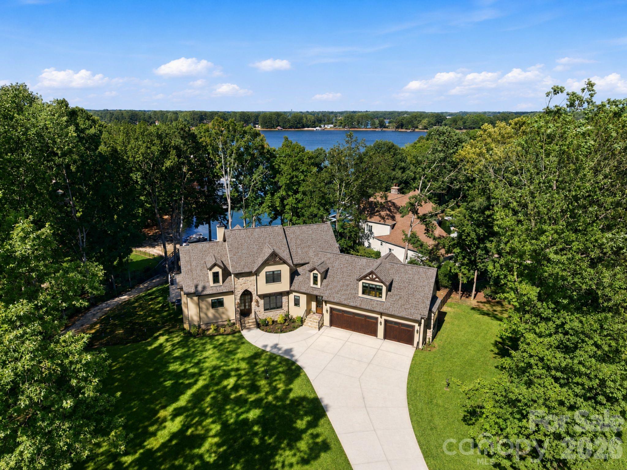 Experience refined lakefront living on Lake Norman, where timeless craftsmanship, elevated design, and resort-style amenities come together in one exceptional estate. Set on approximately one acre with beautiful lake-front views, this 5-bedroom, 6-bathroom residence offers an impressive blend of elegance, comfort, and everyday livability.

From the moment you enter, soaring ceilings, exposed wood beams, expansive windows, and abundant natural light create a dramatic yet inviting atmosphere. The main living area is anchored by a stone fireplace and framed by walls of glass that draw your eye toward the lake, seamlessly connecting indoor and outdoor living. Rich architectural details, custom built-ins, designer lighting, and warm wood accents add character and sophistication throughout.

The chef’s kitchen is both beautiful and highly functional, featuring custom cabinetry, stone countertops, a large center island, premium appliances, a statement wood range hood, and open sightlines to the dining and living areas. Whether entertaining guests or enjoying a quiet evening at home, the layout is designed for effortless gathering.

The private owner’s suite offers a luxurious retreat with vaulted ceilings, exposed beams, lake views, a fireplace, and a spa-inspired bath complete with a freestanding soaking tub, oversized glass shower, and refined finishes. Additional bedrooms provide generous accommodations for family and guests.

The lower level expands the home’s lifestyle offering with a spacious basement featuring a fireplace, bar, lounge area, and direct access to outdoor living. An elevator provides convenient access between levels, while wellness amenities including a steam room and sauna create a true private retreat.

Outdoor living is a defining feature of this property. The lakeside setting offers a spectacular backdrop for relaxing or entertaining, with expansive patio space, mature trees, and an resort-style pool experience overlooking the water. With its rare combination of privacy, scale, lake frontage, and luxury amenities, this Lake Norman estate delivers an extraordinary lifestyle in one of North Carolina’s most desirable waterfront settings.