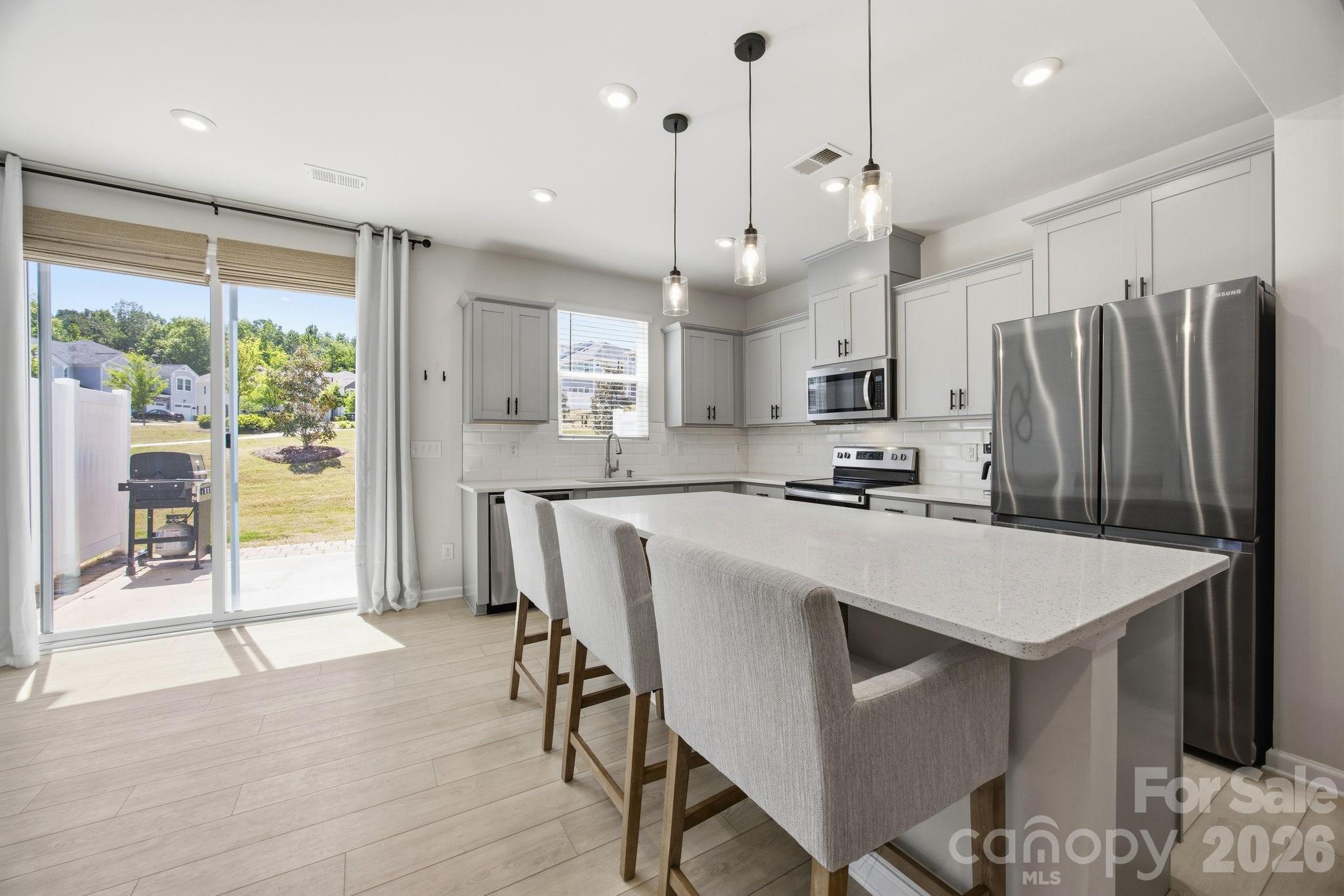 Welcome to this beautifully appointed townhome where comfort, style, and low maintenance living come together effortlessly. The home makes a welcoming first impression from the moment you arrive. Step inside to a thoughtfully designed foyer featuring a built in niche with shelving and an outlet, offering a perfect place for everyday essentials, whether it is a soft glow from a favorite lamp or a convenient spot to keep devices charged and ready as you head out the door. From there, the home opens into a spacious living room that feels both inviting and connected, flowing seamlessly into the kitchen and dining area, an ideal setting for everything from quiet evenings to gathering with friends and family. At the heart of the home, the kitchen is as beautiful as it is functional. Modern gray craftsman style cabinetry, quartz countertops, and a timeless subway tile backsplash set the tone. While the large center island with pendant lighting invites conversation, casual meals, and lingering moments. The sink overlooks the rear yard, offering a peaceful backdrop to your daily routine. Just off the kitchen, the dining area, anchored by a lovely accent wall, opens to the extended patio with privacy screens on each side. Backing to a common area, the outdoor space feels open and expansive, like a natural extension of your home, perfect for morning coffee, evening unwinding, or weekend get togethers. Upstairs, the primary suite offers a true retreat, overlooking the serene rear yard and designed for rest and relaxation. The ensuite bath features a double vanity, upgraded tile flooring, and an expanded tiled shower with a bench seat and transom window that brings in soft, natural light. A spacious walk in closet completes the suite. Two additional bedrooms provide flexibility for guests, work from home needs, or growing households, while the hall bath with double vanity and the conveniently located upstairs laundry room make daily living that much easier. Thoughtful touches like a walk-in linen closet and upgraded open stair railing enhance both function and the light, airy feel throughout. The attached one car garage is a flexible space currently used as a home gym, ready to adapt to your lifestyle. This townhome is ideally located just moments from Lake Wylie, McDowell Nature Preserve, and Rivergate Shopping Center so get ready to enjoy easy access to outdoor recreation, dining, and everyday conveniences. Move right in and start enjoying a carefree lifestyle just in time for summer.