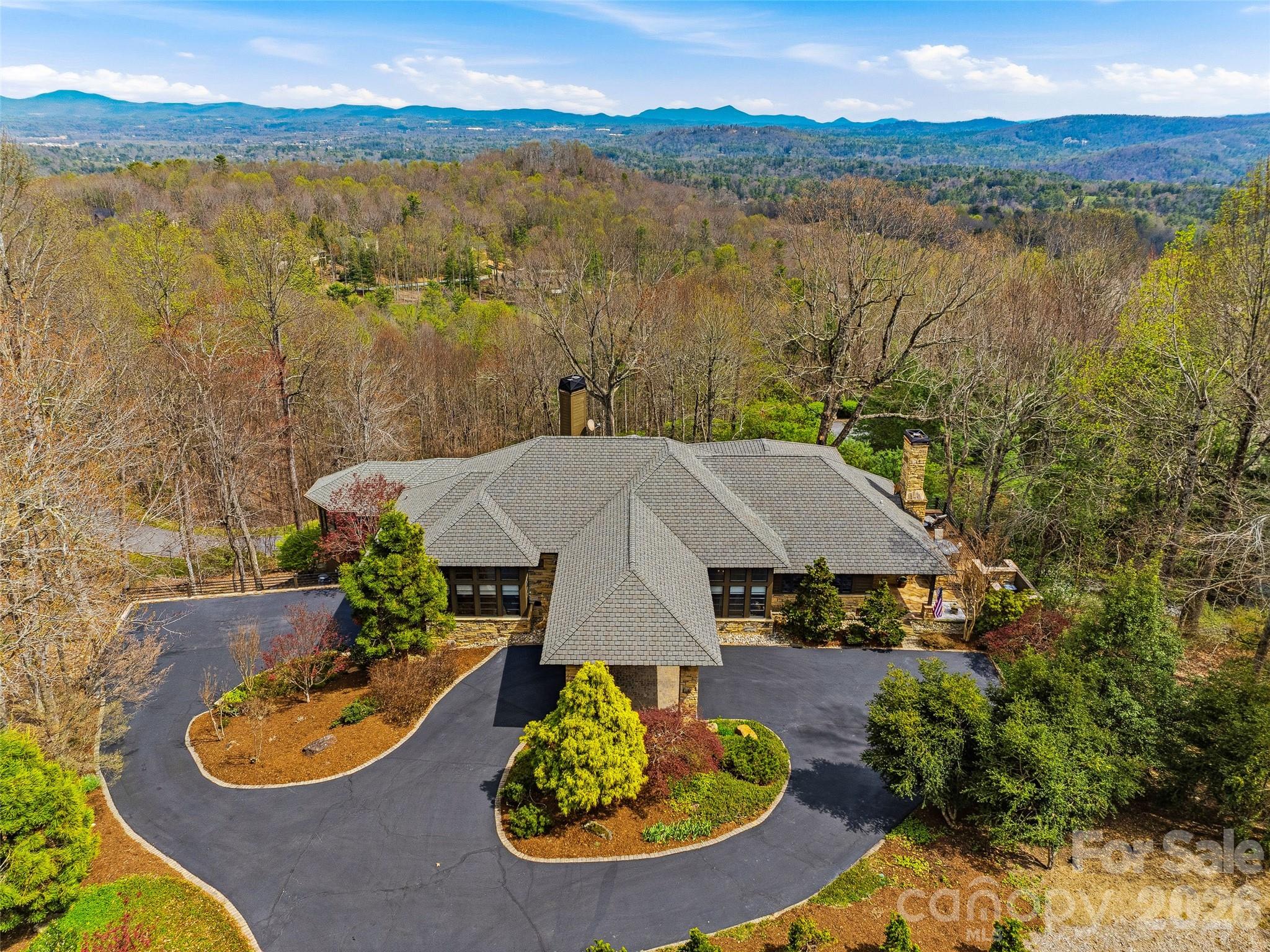 In the misty Blue Ridge Mountains, this exceptional residence, featured in Carolina Architecture & Design and Southern Living, blends the timeless influence of Frank Lloyd Wright with serene, Zen-inspired simplicity. Designed for main-level living, every space is thoughtfully positioned to capture breathtaking views and connect seamlessly with the surrounding landscape. The home flows effortlessly between refined interiors and natural beauty. At its heart, the chef’s kitchen is complemented by a sun-filled breakfast area and inviting hearth room, perfect for quiet mornings by the fire. The Great Room offers a dramatic setting for entertaining, featuring soaring architectural lines, a wood-burning stone fireplace, walk-behind bar, and direct access to a screened porch where mountain air, long-range vistas, and twinkling evening lights create an unforgettable backdrop. A private study with built-ins overlooks beautifully landscaped gardens, while the main-level primary suite provides comfort, privacy, and true single-level living. The lower level, accessible by elevator or stairs, is designed for relaxation and guests and features a spacious family room with a stone fireplace, two bedrooms, two full baths, and a bar area. A standout feature is the fully enclosed, resort-style “pool house” addition by Blue Stone Construction, a stunning cedar-and-glass retreat dedicated to wellness and recreation. Enjoy a heated pool, hot tub, sauna, full bath, fitness center, private putting green, and seamless access to outdoor living spaces. A rare offering where architecture, luxury, and mountain living come together in perfect harmony, set within the prestigious Champion Hills community, home to Tom Fazio’s “Mountain Masterpiece,” and just 8 minutes from historic downtown Hendersonville.