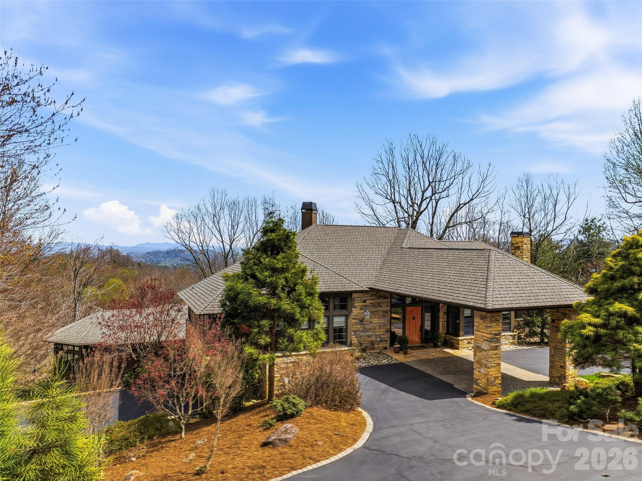 In the misty Blue Ridge Mountains, this exceptional residence, featured in Carolina Architecture & Design and Southern Living, blends the timeless influence of Frank Lloyd Wright with serene, Zen-inspired simplicity. Designed for main-level living, every space is thoughtfully positioned to capture breathtaking views and connect seamlessly with the surrounding landscape. The home flows effortlessly between refined interiors and natural beauty. At its heart, the chef’s kitchen is complemented by a sun-filled breakfast area and inviting hearth room, perfect for quiet mornings by the fire. The Great Room offers a dramatic setting for entertaining, featuring soaring architectural lines, a wood-burning stone fireplace, walk-behind bar, and direct access to a screened porch where mountain air, long-range vistas, and twinkling evening lights create an unforgettable backdrop. A private study with built-ins overlooks beautifully landscaped gardens, while the main-level primary suite provides comfort, privacy, and true single-level living. The lower level, accessible by elevator or stairs, is designed for relaxation and guests and features a spacious family room with a stone fireplace, two bedrooms, two full baths, and a bar area. A standout feature is the fully enclosed, resort-style “pool house” addition by Blue Stone Construction, a stunning cedar-and-glass retreat dedicated to wellness and recreation. Enjoy a heated pool, hot tub, sauna, full bath, fitness center, private putting green, and seamless access to outdoor living spaces. A rare offering where architecture, luxury, and mountain living come together in perfect harmony, set within the prestigious Champion Hills community, home to Tom Fazio’s “Mountain Masterpiece,” and just 8 minutes from historic downtown Hendersonville.