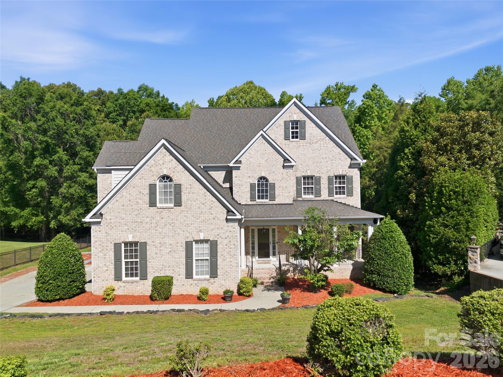 Elegance, scale, and thoughtful design converge in this exceptional 5-bedroom residence nestled in a cul-de-sac. The stately presence of the home is immediately evident, with its full brick construction, side-load two-car garage, and classic rocking chair front porch. As you step through the grand foyer, you’re greeted by rich hardwood floors, intricate crown molding, chair rail, and wainscoting—a testament to the craftsmanship that permeates the entire home. At the heart of the home lies the great room, featuring a high ceiling and expansive windows that flood the space with natural light. A main-level guest suite offers privacy and comfort, complete with a full bathroom.Upstairs, the spacious primary bedroom suite boasts a tray ceiling, serene sitting space, and an extraordinary two walk-in closets. The garden tub provides a corner soaking tub with shower, dual vanities, and a private water closet. Additional accommodations include three generously sized secondary bedrooms, a shared bath with dual vanities. The basement that houses a fully functioning kitchen, washer and dryer, full bath, a bonus room, and living area. Alternatively, the basement can be transformed into a media space, fitness room, or outdoor living area.
Beyond, a deck and extended patio overlook a beautiful private backyard, perfect for entertaining or enjoying quiet evenings at home. Every detail of this home has been thoughtfully designed to offer a seamless blend of luxury, comfort, and functionality, creating a residence that truly stands apart