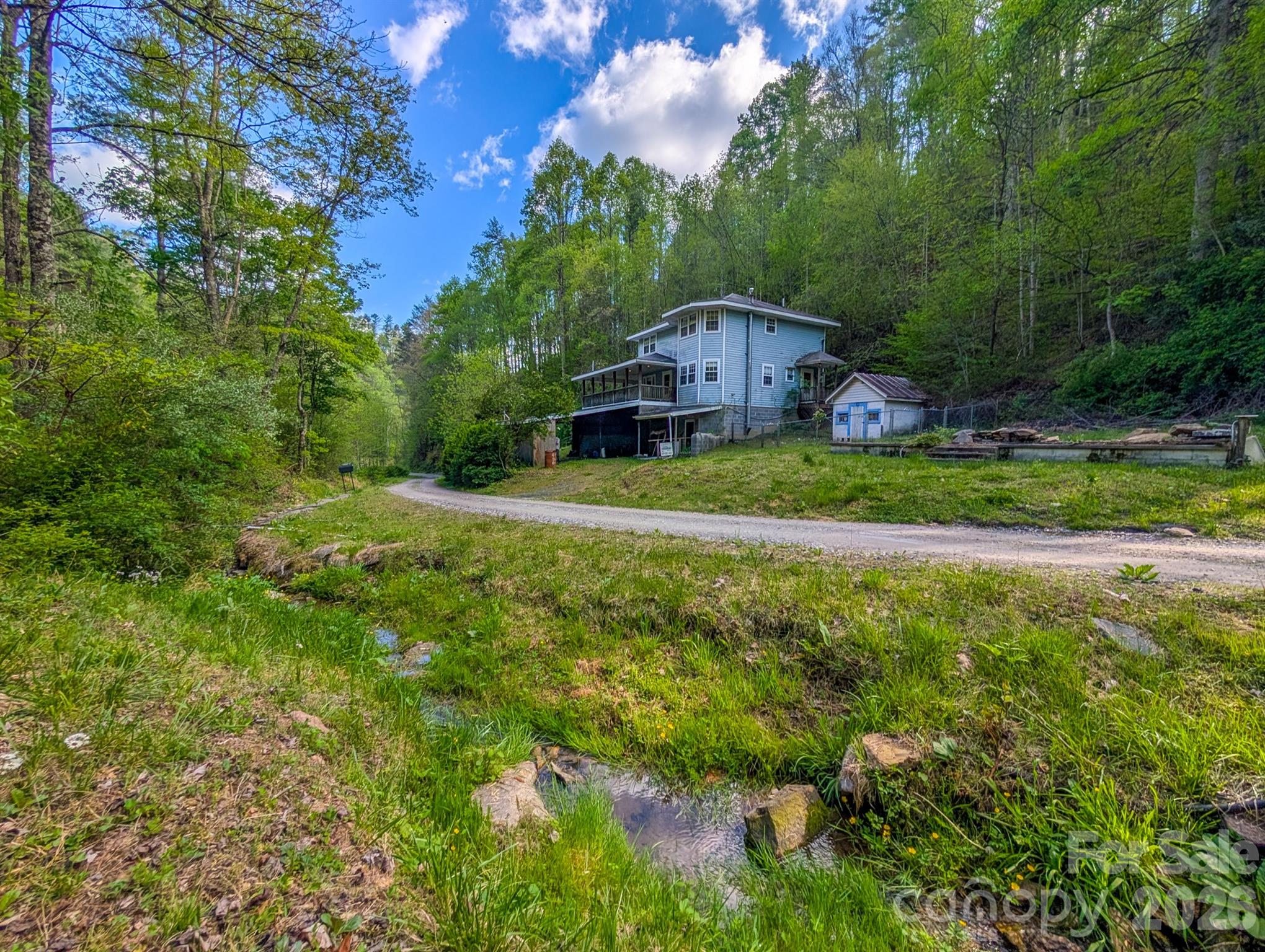 Welcome to 77 Griffith Branch Road, a peaceful mountain retreat set on 15.5+/- acres of wooded, untimbered land with a soothing creek just across the gravel road. Located in the Bradshaw Township of Mitchell County, this 2BR/1.5BA contemporary-style home offers both privacy and potential—an excellent opportunity for someone ready to bring new life to a cherished family property. Built in 1993 and lovingly known for generations as “Nanny & Big Papa's house in the mountains,” the home features a two-story layout with an unfinished basement, ideal for future workshop space or garage parking. The basement includes a propane wall heater and interior stairs leading to the main level. The main floor offers a galley-style kitchen, cozy but spacious living area with gas log fireplace and window A/C unit, a half bath, laundry/mud room for convenience, and an additional flexible room with a bay window—perfect for a dining room, den, office, or hobby space. A kerosene monitor heater provides supplemental heat. Step out onto the covered front porch, which wraps around to the side and connects to a ramped entry and fenced back yard—a wonderful place to listen to the creek and enjoy the surrounding woods. Upstairs you’ll find a large primary bedroom with bay window overlooking the property, a full bath, an additional bedroom, a bonus room, and a small storage/utility room. Pull-down attic stairs add even more storage options. Multiple heat sources are installed, including an oil furnace, kerosene monitor, propane gas logs, and propane wall heater in the basement. An older central vacuum system and an unused wood stove/furnace in the basement convey in as-is condition with no representation from seller. The land offers a mix of level area around the homesite and steep-to-sloping wooded acreage rising behind the property. An old slab foundation from a previous home still remains. Across the road, additional acreage includes an old barn beside the creek—an ideal spot for a picnic or quiet relaxation. A semi-circle driveway, attached drive-through carport, and basement garage bay add convenience. The property includes two wells (one currently in use; the second ris not in use), plus owned oil, propane, and kerosene tanks. A small shed also conveys. Everything in the home conveys unless otherwise arranged. The home was inherited and the current owner has not lived on the property. Located approximately 25 minutes to Burnsville, 22 minutes to Bakersville, and 35 minutes to Spruce Pine, with the North Toe River just minutes away, this property offers the tranquility of mountain living while still being close to town amenities. Whether you’re searching for a year-round residence or a peaceful vacation retreat, this unique property invites you to create your own mountain memories. No survey on record can be found, buyer is recommended to have survey done to confirm acreage - acreage listed is per Deed.