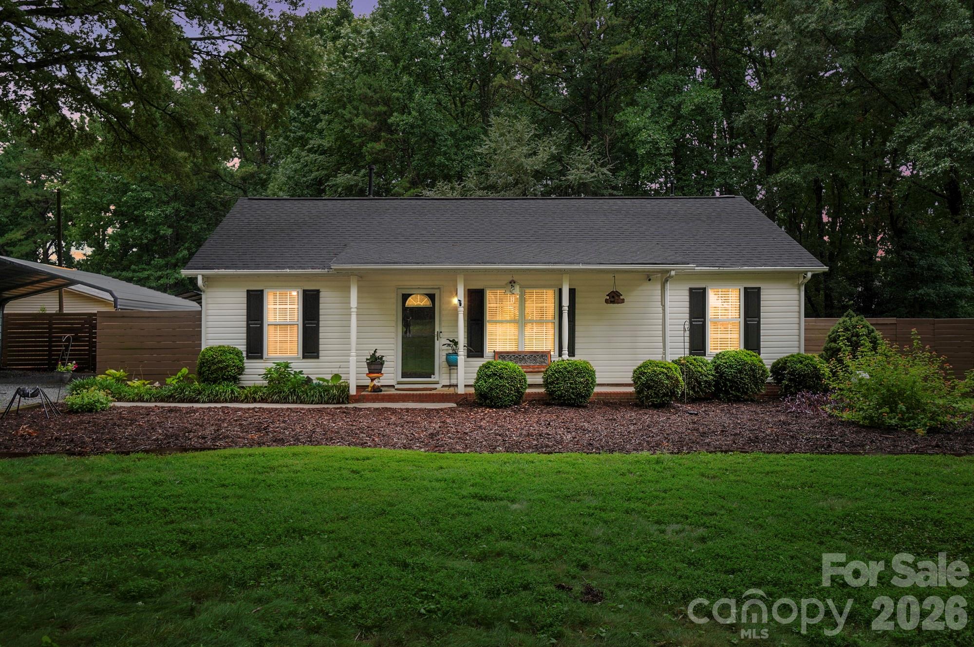 Rare opportunity to own a meticulously maintained 3-bedroom, 2-bath ranch nestled on nearly ¾ of an acre in the heart of Mint Hill. With no HOA and just a short walk to downtown, it's a combination that's hard to come by. Mulched front garden bed, mature shade trees, and a welcoming covered front porch add to the home's charm. Inside, the vaulted living room creates an open, airy feel, while laminate wood and tile flooring provide easy maintenance. Thoughtful details like shiplap ceilings in select spaces, ceiling fans in every bedroom, and a walk-in closet with built-in organization system in the primary suite add character and functionality throughout. The kitchen features stainless steel appliances, updated cabinet hardware, and a bright eat-in dining area with sliders to the spacious backyard. Outside, you'll find a freshly stained deck with gazebo, stone patio, tranquil water feature, and private wooded surroundings—a great place to relax or entertain. Additional features include an oversized two-car covered carport, an extended driveway with plenty of parking, and two storage buildings. Gutter guards, a 2021 roof, 2020 HVAC, and 2018 water heater provide added peace of mind for the next owner.