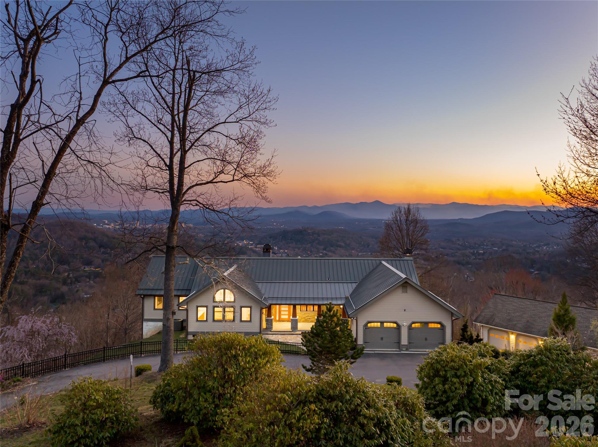 Perched on a generously sunny high plateau over 7.11 private acres, this architectural gem offers stunning panoramic views of Asheville, the iconic Blue Ridge Mountains, and Mount Pisgah behind Biltmore. A unique opportunity to be ten minutes from fine dining and shopping, and also cycle to The Blue Ridge Parkway. The immense beauty of traveling north of town up Elk Mountain, designated in the 1930s as 'NC Scenic', remains remarkable. This custom-designed home is tucked behind a private gated circular driveway and has been lovingly updated over the decades. The epitome of refined mountain living embraces the seasons as operable walls throughout the home blur the lines between indoor and outdoor spaces. Experience dawn over Tanbark Ridge & Town Mountain to the east as you sip coffee from your bedroom suite with red-tailed hawks flying below. As the day progresses, find yourself having dinner & cocktails at the other end of the home as you become one with the sunset, just before Asheville's twinkling lights perform. This legacy estate is more than a residence; it is a retreat. Custom-designed for entertaining, the great room and massive stone fireplace spill into a breathtaking open-designed, extraordinary chef's kitchen. The personal resting wing of the home is a beautiful combination of a wormy chestnut library and modern luxurious sensibilities; extraordinary bathing rooms and large closets. The downstairs family/guest quarters offer privacy, big views, and outdoor access. Walk among fruit trees to a detached greenhouse and expansive 6-car garage, which could be transformed into a creative studio space or workshop.