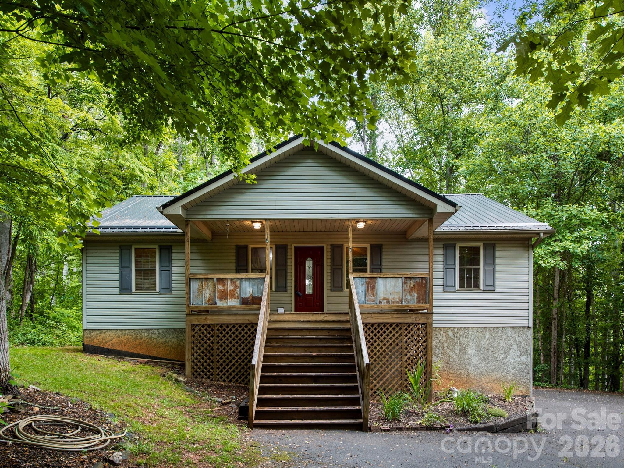 Tucked away in the peaceful woods of Candler, this inviting home offers the perfect blend of comfort, character, and mountain privacy. From the moment you arrive, the circular driveway and natural setting create a welcoming sense of retreat. Inside, beautiful hardwood floors, warm reclaimed local wood accents, and a cozy propane gas fireplace give the home a rustic elegance and timeless charm that’s difficult to find. The home features a new metal roof installed in 2025, rear deck boards replaced in 2025, and updated AC components outside, including the blower replaced in 2020. The spacious lower-level den with half bath offers endless possibilities for entertaining, movie nights, hobbies, a game room, or guest space, while the oversized two-car garage provides plenty of room for storage, tools, or outdoor gear. Step outside and enjoy the beauty and privacy of the wooded backyard, and there's also a fire pit area in the front that's perfect for cool mountain evenings under the stars. Whether you’re enjoying coffee on the deck, gathering around the fire with friends, or relaxing by the fireplace after a long day, this home offers the kind of atmosphere that simply feels good to come home to. All appliances convey. Home is served by a shared well with the added security of a propane-powered backup generator for the well system. Shared driveway access with a private circular drive for the home.