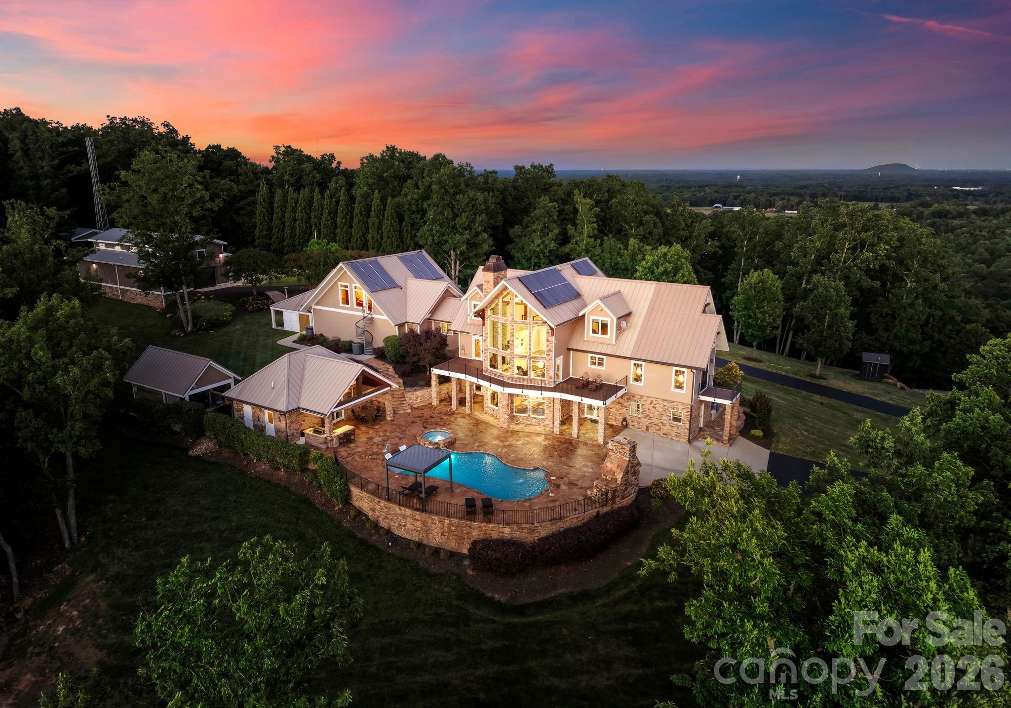 Have you ever seen the Charlotte skyline and Blue Ridge Mountains from one breathtaking vantage point? Perched atop Pasour Mountain on more than 100 private acres, 605 Recore Ridge delivers an extraordinary perspective few properties in the Carolinas can offer. Over a mile of paved private driveway across the top of Pasour Mountain providing separate gated access to main roads on both sides of the property. With panoramic sky views stretching from the glittering Charlotte skyline to the distant peaks of the Blue Ridge Mountains, this mountaintop sanctuary is among the region’s most remarkable luxury estates. Built in 2012, the residence was thoughtfully designed to blend refined luxury, self-sufficiency, and unmatched natural beauty. The main level features a luxurious primary suite alongside a gourmet chef’s kitchen appointed with premium Bosch, Viking, and Sub-Zero stainless steel appliances. Expansive living spaces are framed by endless vistas and designed for both intimate living and exceptional entertaining. The upper level offers additional guest suites, while the fully finished lower level includes a private guest retreat, sauna, fitness room, and direct access overlooking the resort-style saltwater pool and mountain views beyond. Outdoor living is equally impressive with a pool house complete with full kitchen and bath, outdoor kitchen, covered overlook pavilion, serene pond, barn, and unforgettable sunset views that transform every evening into an experience. Designed with long-term sustainability and preparedness in mind, the estate features solar panels supporting heat and water systems, heated floors throughout, whole-house generator, and infrastructure intentionally built to function independently during natural emergencies. The attached three-car garage is complemented by upper-level recreation and living quarters with a Murphy bed, plus a separate workshop garage offering exceptional flexibility.
From the professional workshop spaces to the expansive grounds and private retreat-like setting, every detail was carefully considered to create a property unlike anything else in the region. Offering complete privacy while remaining a convenient drive to Charlotte, this is more than a luxury home — it is a fully realized mountain estate designed for elevated living without compromise.