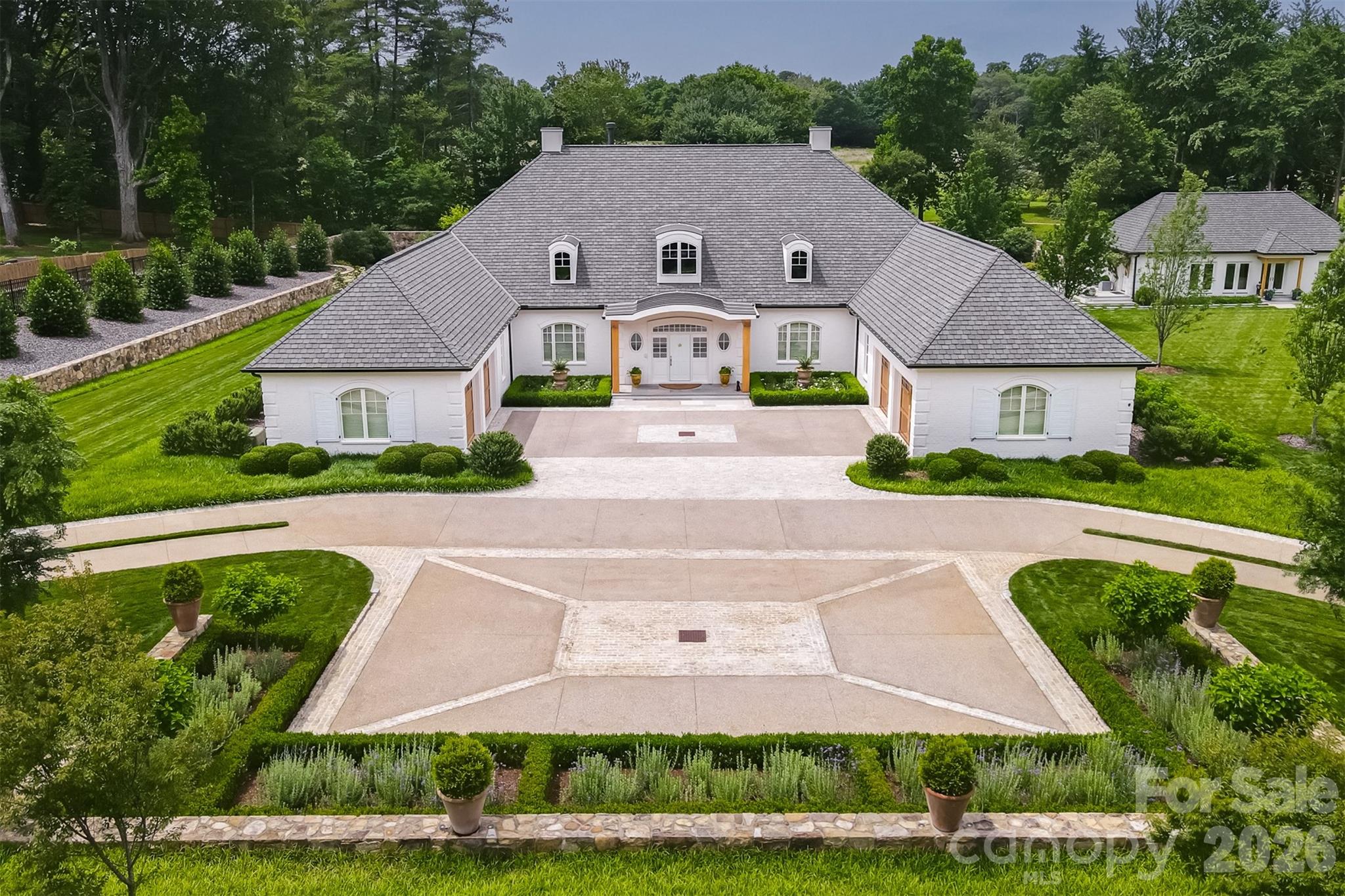 This sophisticated one-story home epitomizes quality and craftsmanship rarely seen! The main house features large open living spaces, fabulous primary suite with sumptuous marble bath and unbelievable dressing room. The living room opens to a large porch with fireplace overlooking the Reynolda Estate. Dining room with custom built-ins and glamorous lacquered ceiling. The kitchen is lined with custom cabinetry and top of the line appliances, breakfast room and fully equipped pantry. Two guest rooms each have ensuite baths and are discreetly situated away from the primary suite.  The idyllic swimming pool and cabana offer wonderful outdoor entertaining opportunities. A fully self-contained guest cottage houses a pool bath, vaulted open living space with a fully equipped kitchen, bedroom, additional bath, and laundry. The distinctive design offers a motor court and separate double garages. The exquisite landscape was designed by Jeff Allen and is fully fenced and gated. True masterpiece!