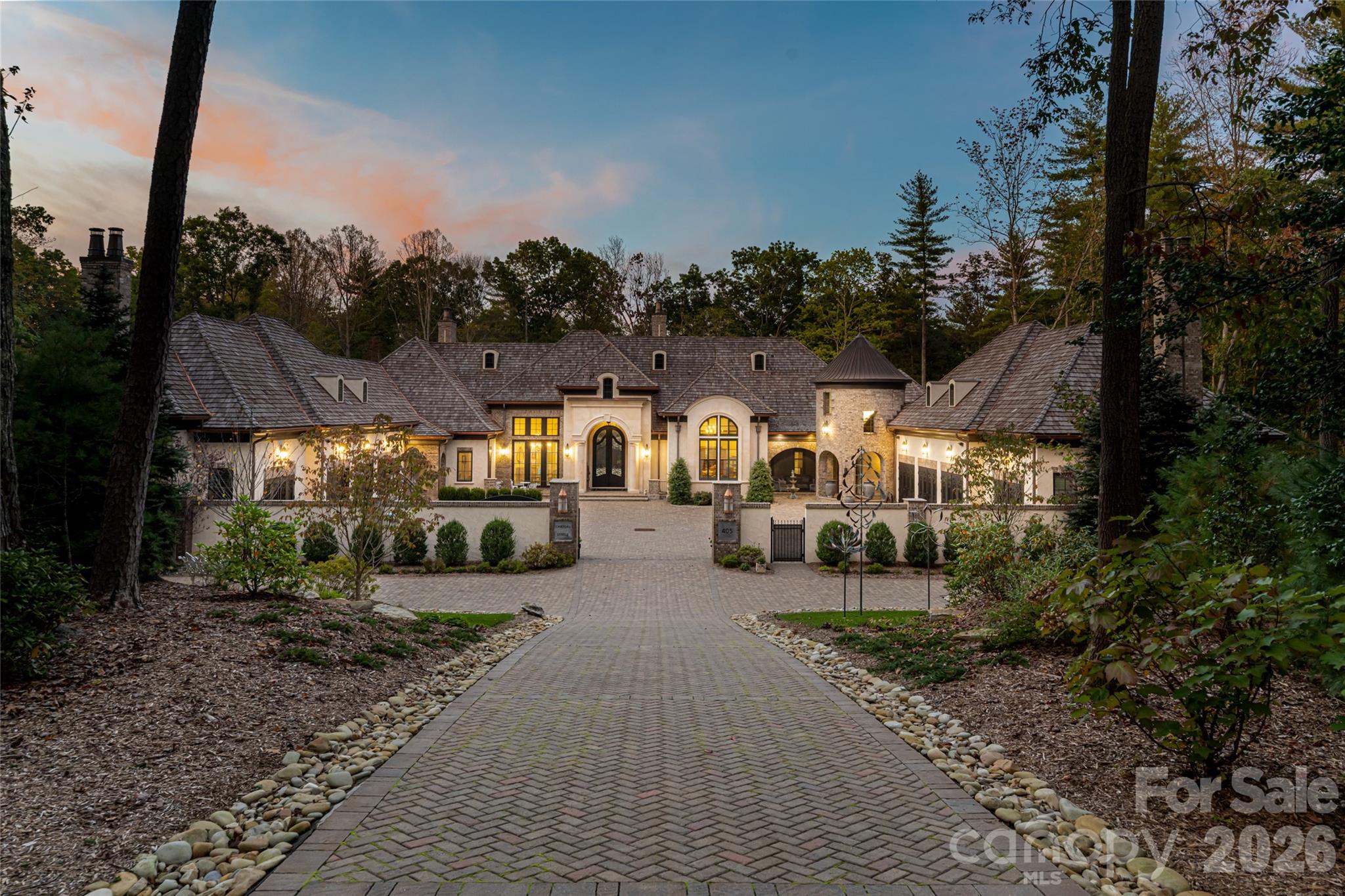 Behind private gates within the prestigious Ramble Biltmore Forest, 405 Ramble Way is an extraordinary estate inspired by the enduring traditions of timeless architecture and exceptional design. Surrounded by meticulously curated gardens and lush native landscaping, the property offers a rare sense of serenity where nature and craftsmanship exist in harmony. A stately cast stone entrance sets the tone for the home beyond, where every space unfolds with quiet grandeur and refined elegance. Masterfully constructed without compromise, the residence is defined by impeccable craftsmanship and an extraordinary palette of enduring materials, including cast stone, reclaimed timber beams, hand-forged ironwork, exotic granite, a cedar shake roof, six exquisite marble and natural stone fireplaces, and a custom glass ceiling that bathes the solarium in natural light. Designed to honor everyday living and unforgettable entertaining, the home's gracious floor plan balances intimate family spaces with dramatic architectural moments. The magnificent grand salon is the heart of the residence, where soaring 28-foot windows and reclaimed wood beams create an atmosphere of warmth and scale while framing tranquil views of the surrounding forest, inviting the beauty of the landscape indoors. Every detail has been thoughtfully considered to enrich the experience of living here. A charming brick-paver pathway meanders around the home, encouraging peaceful walks through the beautifully landscaped grounds and offering ever-changing perspectives of the estate's gardens and woodland setting. For the automotive enthusiast or discerning collector, an extraordinary heated and cooled eight-car garage, equally suited as a private car museum, provides an exceptional showcase for prized vehicles while complementing the home's uncompromising standard of luxury. Elegant yet inviting, grand yet deeply livable, 405 Ramble Way is more than a remarkable residence, it is a private sanctuary where timeless craftsmanship, architectural distinction and the natural beauty of Biltmore Forest come together in balance.