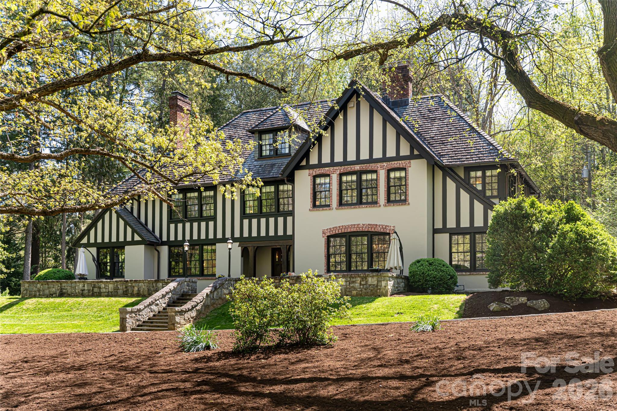 Directly across from the storied Biltmore Estate, this distinguished English Tudor blends historic character with modern comfort. Tucked along a quiet, non-through street and framed by mature trees, the setting feels private and timeless. Inside, rich wood floors, arched doorways and leaded-style windows reflect enduring craftsmanship, while thoughtful updates bring ease to daily living. The renovated kitchen, with custom cabinetry, stone countertops and premium appliances, is equally suited to casual mornings and elegant entertaining. Incredible renovation throughout. Upstairs, the primary suite offers a peaceful retreat, joined by three additional bedrooms and a versatile third-floor space ideal for guests or creative pursuits. A charming guest cottage and updated gardener’s shed provide added flexibility. Manicured gardens and a gated entry complete this rare offering just moments from Asheville’s most iconic landmark.
