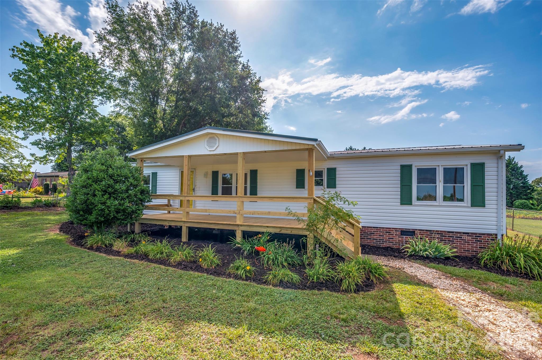 Welcome home to this beautifully maintained 3-bedroom, 2-bath doublewide situated on a spacious 0.69-acre lot. This inviting home features an eat-in kitchen complete with stainless steel appliances, offering the perfect space for everyday meals and entertaining. The primary suite is a true retreat with a large ensuite bathroom featuring a relaxing garden tub, separate stand-up shower, and a generous walk-in closet.  Step outside to enjoy the large fenced backyard, perfect for pets, play, or gatherings. The property also includes two outbuildings for additional storage or workshop space.Relax on the charming rocking chair front porch overlooking the beautifully landscaped yard. Additional highlights include a paved driveway and updated windows, providing both curb appeal and energy efficiency.With plenty of indoor and outdoor space, this move-in-ready home offers comfort, convenience, and country-style living with modern updates.