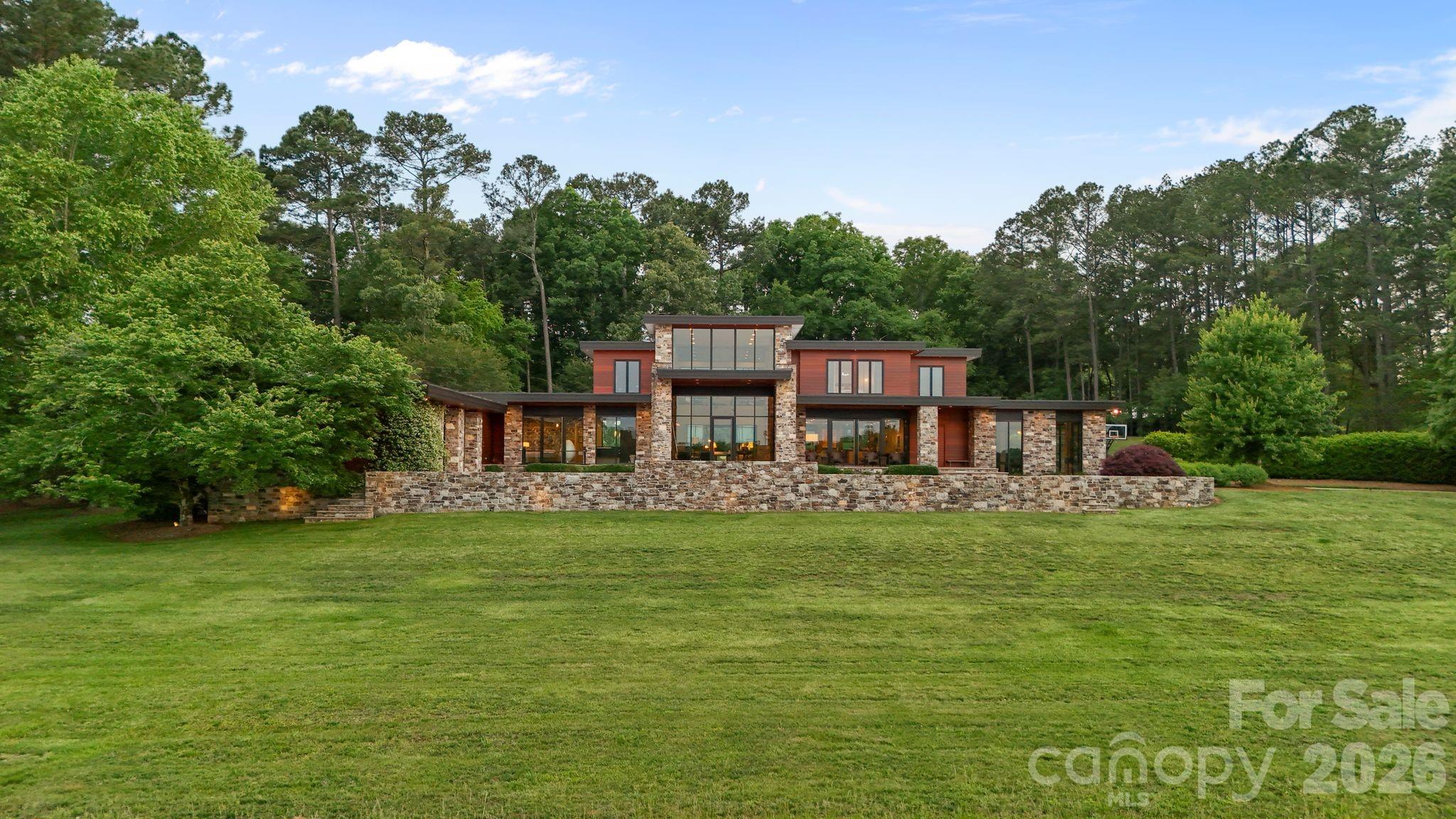 THE RANCH AT FAIRES RD: A Modern Equestrian Estate. Set quietly beyond the pace of Charlotte, this 75+ acre modern ranch estate offers a rare expression of architectural intention and landscape harmony. Conceived by Frank Smith after years of immersive study in contemporary design, and brought to life with interiors by Barrie Benson and craftsmanship by Kingswood Custom Homes, the home is both a personal retreat and a considered work of modern architecture.

The approach is deliberate—a sweeping motorcourt, anchored by a sculptural fountain, sets a tone of understated grandeur. Inside, the residence unfolds through volumes of glass and stone, where light becomes a defining material. Floor-to-ceiling storefront windows and pivoting glass doors dissolve the boundary between interior and landscape, opening to a composition of water, sky, and rolling acreage.

At the heart of the home, materials are both tactile and restrained—wide-plank black walnut floors, flamed leathered granite, and precision-crafted cabinetry that reveals itself at the touch. A curated Miele kitchen suite balances performance with quiet elegance, designed as much for gathering as for function.

The primary suite is conceived as a private pavilion, complete with a steam shower and an intimate outdoor bathing terrace—an experience that invites stillness and connection to the surrounding landscape.

Beyond the walls, the estate unfolds as an immersive environment. A heated pool with integrated current system allows for both leisure and training, while a private pond—stocked for bass and brim fishing—reflects the changing light of day. A driving range introduces a refined recreational element, complemented by expansive acreage suited for skeet shooting, four-wheeling, and dirt biking along established trails. Thoughtfully integrated into the landscape, the property offers a dynamic outdoor lifestyle—equally suited for quiet moments in nature and more active pursuits across the land.

The equestrian component is equally considered, designed to resonate with discerning equestrians and those drawn to a refined rural lifestyle. A well-appointed barn serves as both a functional working stable and a natural extension of the estate, offering four stalls, a dedicated tack room, and lofted hay storage for efficient daily operation. A covered equipment shed provides seamless access to vehicle storage and groundskeeping implements, supporting the stewardship of the land.

The surrounding acreage lends itself naturally to multiple fenced pastures and paddocks, allowing for thoughtful rotation, while rolling terrain and open sightlines create an ideal setting for private riding trails—suited for both leisurely rides and more focused training within the privacy of the estate. Enhancing the experience, the barn also incorporates a gym and a thoughtfully appointed kitchen and outdoor lounge space with fire pit, allowing for an effortless transition between training, care, and relaxation.

Integrated technology—via a Savant whole-home system—operates discreetly in the background, orchestrating lighting, climate, and security with precision. A Generac generator, underground propane reserves, and whole-home water filtration reinforce a sense of self-sufficiency.

An additional guest house, offered as-is, presents an opportunity for further personalization.

Located within convenient reach of Charlotte, yet intentionally removed from its immediacy, this estate offers a compelling duality: accessibility and escape. It is a place defined not only by its design, but by the experience it creates—quiet, expansive, and enduring.