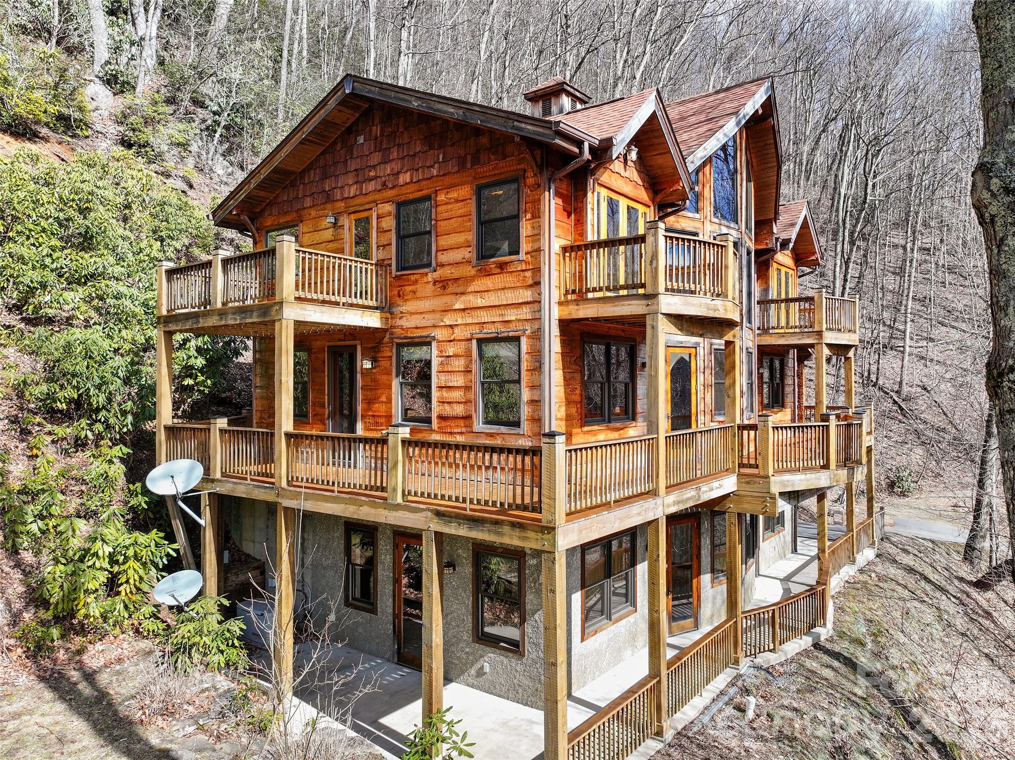 Nestled at an impressive 4,000-foot elevation in the highly desirable Fisher Ridge subdivision—just off the vibrant heart of Maggie Valley, North Carolina—this exquisite custom mountain hand-hewed timber frame cabin offers unparalleled privacy and serenity as an end-of-the-road retreat. Spanning over 3,200 square feet of thoughtfully finished living space across three levels (accessible via a convenient elevator), the home masterfully blends rustic authenticity with modern comfort. The standout living room boasts dramatic 26-foot cathedral ceilings adorned with exposed, hand-hewn beams that showcase the craftsmanship of reclaimed timber, creating an airy, grand atmosphere perfect for gatherings or quiet contemplation. Sunlight pours in through expansive windows, highlighting the direct southern exposure that bathes the interiors in natural warmth year-round and frames breathtaking mountain vistas. The spacious eat-in kitchen serves as the home’s welcoming core, featuring ample cabinetry, a generous pantry for storage, and seamless flow into the dining area—ideal for casual family meals or entertaining. Rich, character-filled flooring sourced from a 100+ year-old cotton barn adds timeless texture and history underfoot, complementing the vaulted ceilings throughout. Additional living spaces include a cozy library for reading nooks, a dedicated home office for productivity, and a versatile family room for relaxation or media enjoyment. The layout provides 2 bedrooms plus a flexible bonus room, supported by 3.5 well-appointed bathrooms that ensure comfort for owners and guests alike. Outdoor living is elevated to an art form with a expansive wraparound deck (trim out your own views) offering multi sweeping views and multiple seating areas, accented by two charming upper-level Juliette balconies for intimate moments overlooking the landscape. The home’s thoughtful design embraces the mountain lifestyle, with energy independence assured by a Generac whole-house generator, while pay-for-access utilities maintain low-maintenance ease. A single-car garage provides protected parking, and the property’s secluded positioning delivers true end-of-the-road privacy amid the peaceful, wooded surroundings of Fisher Ridge—renowned for its scenic appeal, community charm, and proximity to Maggie Valley’s dining, shopping, golf, and outdoor adventures, including quick access to the Blue Ridge Parkway and Cataloochee area. This rare timber frame gem combines old-world hand-hewn elegance, abundant natural light, and modern conveniences into a luxurious yet soulful mountain escape ready for immediate enjoyment or personalization. (three en suites, two bedroom septic).
