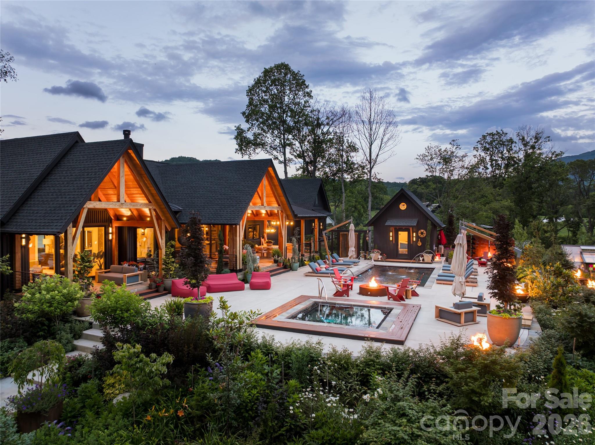 Where high-design industrialism meets a world-class botanical sanctuary, you’ll find this Fairview masterpiece. Conceived by the visionary founders of the Key West Butterfly and Nature Conservatory, this estate is more than a home, it is a 1.89-acre pollinator paradise and a triumph of Modern Industrial Timberpeg architecture, a symphony of steel, glass and timber. Guided by a passion for light and natural geometry, the creators utilized sustainably harvested Douglas Fir timbers and soaring glass to blur the line between interior and the wild. The 3,512-square-foot residence pulses with artisanal energy such as exotic zebra wood cabinetry, walnut wainscoting and hand-forged lighting from Hubbardton Forge and Sonneman. From the chef’s kitchen with Fisher & Paykel appliances to the 19th-century German hunting lodge library hutch, every inch reflects a life dedicated to curated beauty. The living landscape is true to the owners’ legacy and the grounds are a masterclass in eco-stewardship. This isn’t just a garden, it’s a thriving ecosystem. Two buried 5,000-gallon cisterns harvest rainwater to sustain lush perennial beds designed to explode with seasonal color. A climate-controlled timber-frame greenhouse allows for year-round cultivation, while a tranquil waterfall and rockwork set a meditative tone. Even the workspace is inspired, a reimagined metal silo serves as a private office, clad in poplar and walnut. Resort living from home is the theme the creators manifested to create a perfected indoor-outdoor lifestyle. The primary suite dissolves into a pool terrace featuring a water feature, hot tub, and gas fire bowls surrounding the pool and anchored by an oversized gas fire pit. Host beneath a chandelier outdoor dining pavilion or the kitchen terrace, complete with a wood-fired pizza oven and professional-grade outdoor appliances. Guests will find sanctuary in the NY-style ADU perched above the three-bay garage, offering a sleek, modern loft experience with its full kitchen and artisan concrete finishes. Sustainable sophistication in the soul of the home is nature-focused, and the bones are high-tech, including a full-house generator, EV charging, dual tankless water heaters and a fully encapsulated environmental crawlspace. In the desired Clearview community, you are minutes from the pulse of Asheville but in a private, pastoral world where birds and butterflies are your closest neighbors. This is a rare opportunity to own a legacy property built by masters of the natural world.