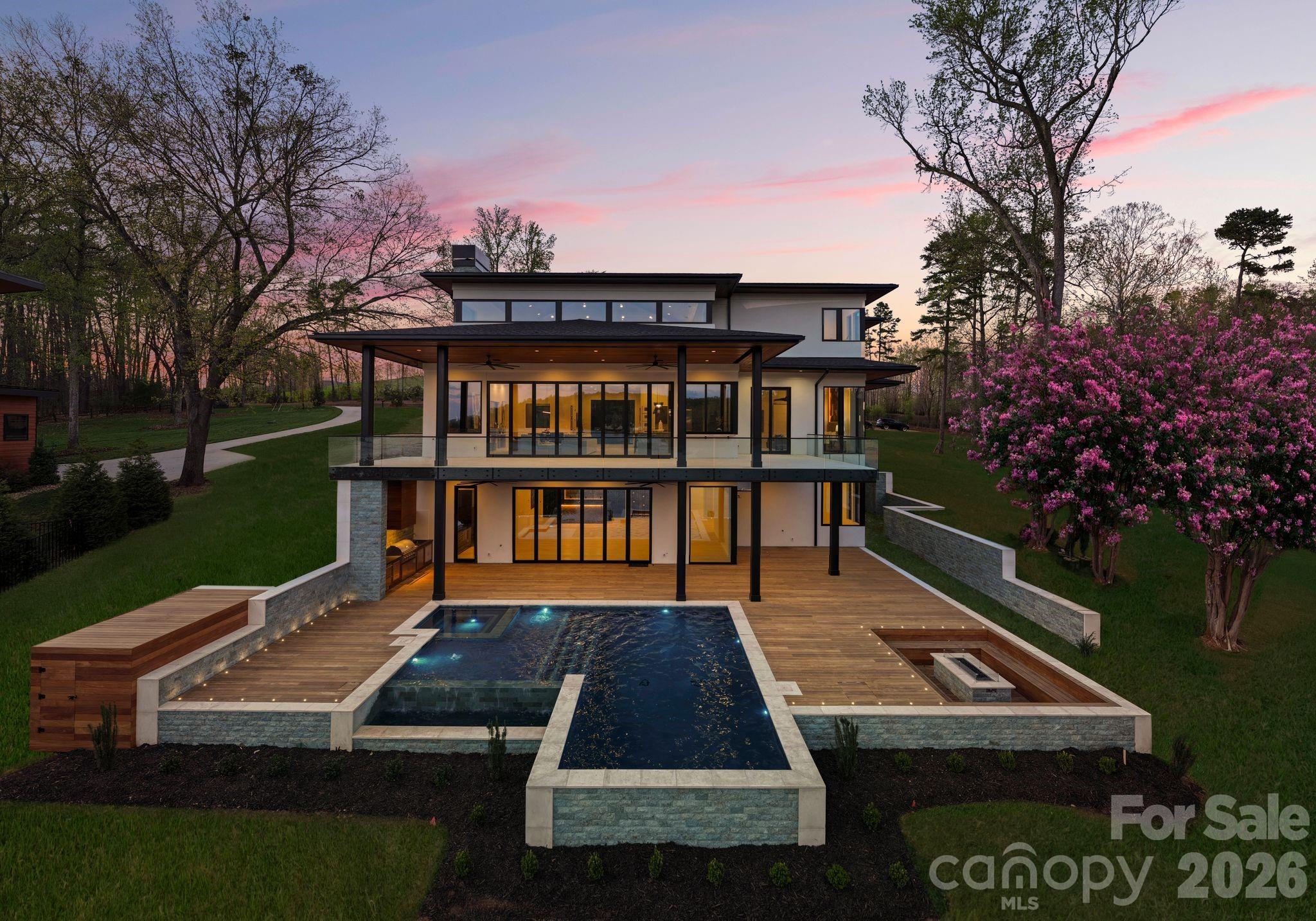 Exquisite Waterfront Masterpiece on Lake Wylie – Discover an architectural wonder just 20 minutes from Uptown Charlotte. Designed and built by Artistic Contractors, one of Charlotte’s premier design/build firms, this 8,300+ sq ft modern lakefront retreat embodies warmth, innovation, and serenity—offering a rare combination of world-class design and unmatched proximity to the city.
Set on a gently sloping waterfront homesite beneath mature trees, this residence blends natural materials with bold geometry to create one of the most extraordinary private homes on Lake Wylie. Located just 5 minutes from Charlotte Douglas International Airport, this property delivers true convenience without compromise.
Step through the monumental 10’ x 10’ pivot door into the breathtaking 1,400 sq ft atrium great room—a soaring, light-filled space combining living, kitchen, and dining beneath a dramatic 28-foot pyramidal clerestory ceiling clad in rich imported Peruvian cumaru wood. Exposed structural steel and a 24-foot folding glass wall seamlessly connect the interior to expansive covered terraces, creating one of the most architecturally striking living spaces in the region.
The 6-bedroom, 5.2-bath home was designed with both luxury and livability in mind. The chef’s kitchen features a 10’ x 6’ waterfall island, professional Monogram appliances, Miele induction cooktop, and a concealed scullery. The great room is anchored by a 74” linear fireplace set against a dramatic wall of book-matched stone and custom wood paneling. A floating mono-stringer staircase with glass railing and 3” white oak treads serves as a sculptural centerpiece.
The primary suite offers a true retreat with floor-to-ceiling glass capturing long-range lake views. The spa-inspired bath features a freestanding tub, oversized rain shower over a cumaru deck floor, and expansive custom closets with integrated lighting.
Outdoor living is equally impressive, with over 1,800 sq ft of covered terraces finished with cumaru ceilings and imported Indonesian limestone flooring. Motorized screens, built-in audio, and a full outdoor kitchen create a seamless extension of the home. The resort-style infinity-edge pool and spa, finished in sukabumi stone, overlook Lake Wylie and are surrounded by thoughtfully designed landscape elements.
Additional features include all-aluminum thermally broken windows and doors with low-E argon-filled 1" thick glass, spray foam insulation, tankless hot water, smart home integration, EV-ready three-car garage, and lake-fed irrigation system.
Situated among a collection of high-end custom homes, this property represents a rare opportunity to own new construction of this caliber on Lake Wylie—often available at a compelling value relative to comparable homes on Lake Norman—while being just minutes from Uptown Charlotte, the airport, The River District, and nearby walking trails. This is more than a home—it is a statement of design, craftsmanship, and lifestyle.