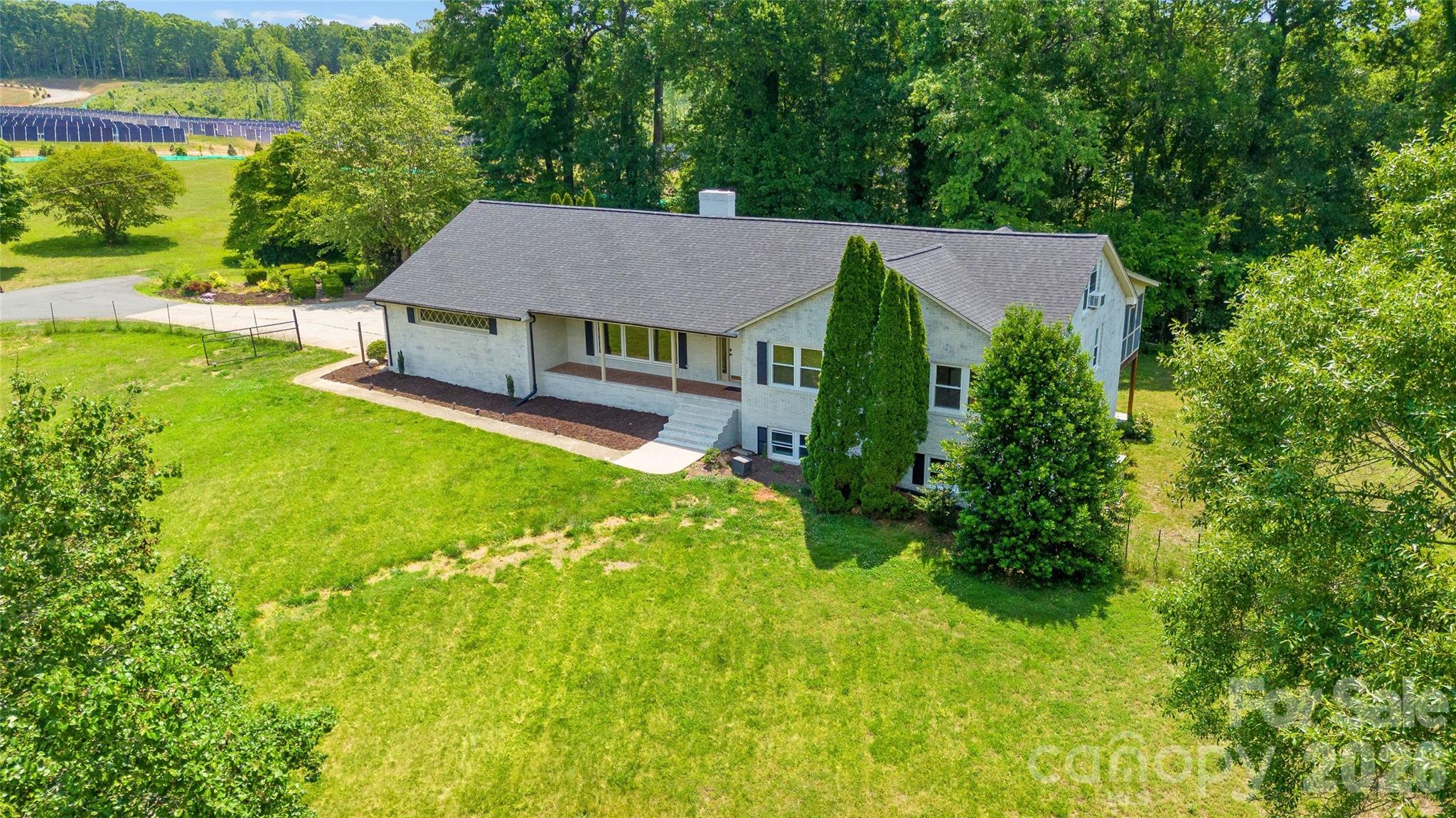 Welcome to 2004 Fountain Lane, a sprawling 4.3-acre brick estate thoughtfully designed for multigenerational living, exceptional privacy, and incredible equestrian potential. Offering 3,915 square feet of living space, this unique ranch-style home perfectly balances shared gathering areas and independent living quarters. From the expansive custom broken-tile front porch, you'll enter the stunning living room, where soaring vaulted ceilings, rich exposed wood beams, and a dramatic floor-to-ceiling stone fireplace create an unforgettable first impression. The kitchen combines timeless character with modern convenience, featuring rich blue cabinetry paired with crisp white finishes to create a modern farmhouse feel. A striking stone accent wall and arched cooking alcove add warmth and architectural charm, creating a distinctive focal point that complements the kitchen's bright, open design and generous workspace. Elegant custom stonework, beautifully renovated bathrooms with updated tile, zero-entry showers, and an expansive chef's kitchen create a warm and sophisticated main living environment. Experience the pinnacle of indoor-outdoor entertainment at the rear of this spectacular home, featuring both a light-filled sunroom, equipped with its own dedicated HVAC system, and a massive lodge-style screened porch. Together, these side-by-side bonus spaces create an unparalleled hosting venue designed to accommodate any event, allowing guests to move effortlessly between the comfort of the sunroom and the open-air, tree-lined sanctuary of the screened porch. With direct access to the screened porch, the spacious primary bedroom serves as a true retreat, featuring an updated bathroom with a custom-tiled, zero-entry shower and walk-in closet. Main-level living is completed by two additional bedrooms and a full bathroom. The fully finished walk-out lower level creates an ideal second living area with exceptional privacy and autonomy. Featuring a spacious family room, a fourth bedroom or private suite, a full bathroom, and a separate lower-level garage, this level is perfectly suited for multigenerational living, long-term guests, hobby space, or home-based work needs. Outside, the property's rolling terrain and more than four private acres provide the ideal canvas for endless possibilities. Expansive open areas offer excellent potential for paddocks, riding arenas, and future equestrian improvements. An existing fenced yard provides a secure space for pets. A storage shed offers immediate space for equipment and supplies, with ample room remaining for a custom barn or additional outbuildings. Despite its peaceful country setting, the property offers convenient access to local amenities, feed stores, veterinary services, outdoor recreation, and major Charlotte-area employment centers. The home is assigned to Catawba Springs Elementary School, East Lincoln Middle School, and East Lincoln High School. Whether you seek a private country estate, a flexible multigenerational home, or a property with exceptional outdoor living and sports potential, 2004 Fountain Lane offers a rare combination of space, versatility, and opportunity.