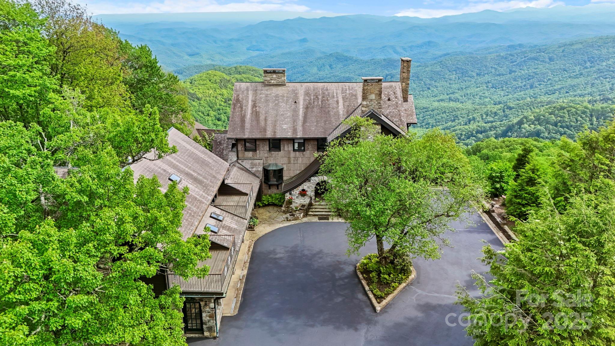 Perched atop a rhododendron-covered ridge in the prestigious Mayview neighborhood, & fronting Pisgah National Forest, Far Horizons is a landmark 1924 estate offering breathtaking, panoramic views stretching over 100 miles- capturing sunsets & Johns River Gorge, Grandfather & Grandmother Mountains, Table Rock, Hawksbill, Sugar, & even the Charlotte skyline on a clear day. Originally built by designer of the famed Mayview Manor & on his choice lot, this masterfully restored residence blends timeless mountain charm w/ modern luxury. Painstakingly renovated down to the studs in '90 & again in '15 (+ upgrades in recent years), the home now has new plumbing, electrical, HVAC, & smart systems. The 5,312 sq.ft. main residence is a celebration of historic architecture & contemporary livability, w/ 7 original stone fireplaces, exposed beams, & walls of windows inviting the outdoors in. The great room w/ massive stone hearth opens to sunroom w/ wet bar, formal dining w/ fireplace, & gourmet chef’s kitchen w/ reclaimed wormy chestnut cabinetry, granite counters, Sub-Zero/Wolf, & breakfast nook. Upstairs, a primary suite = private stone balcony, FP, walk-in closet, & spa-like BA. 3 more ensuite BRs each offer unique views & FPs, 1 w/ private balcony. Lower level = 2nd living, game room & pool table, wine cellar, HBA — perfect for entertaining. A breezeway connects main house to 3 car+ garage & fully-equipped 1,050 sq.ft. apartment w/ kitchen, living, BR, BA, & flex—ideal for guests & multi-generational living. Add'l features: circular driveway, gated entry/ample parking (rare for in-town Blowing Rock), redesigned landscaping (stone patios/paths, gardens); Smart home lighting/sound/HVAC/security; Historic bark siding from original construction; 3,600+ ft elevation = cool summer temps; city water/sewer, proximity to Moses Cone trails. A once-in-a-generation opportunity to own a storied mountain estate that balances history, privacy, convenience, & unforgettable views.