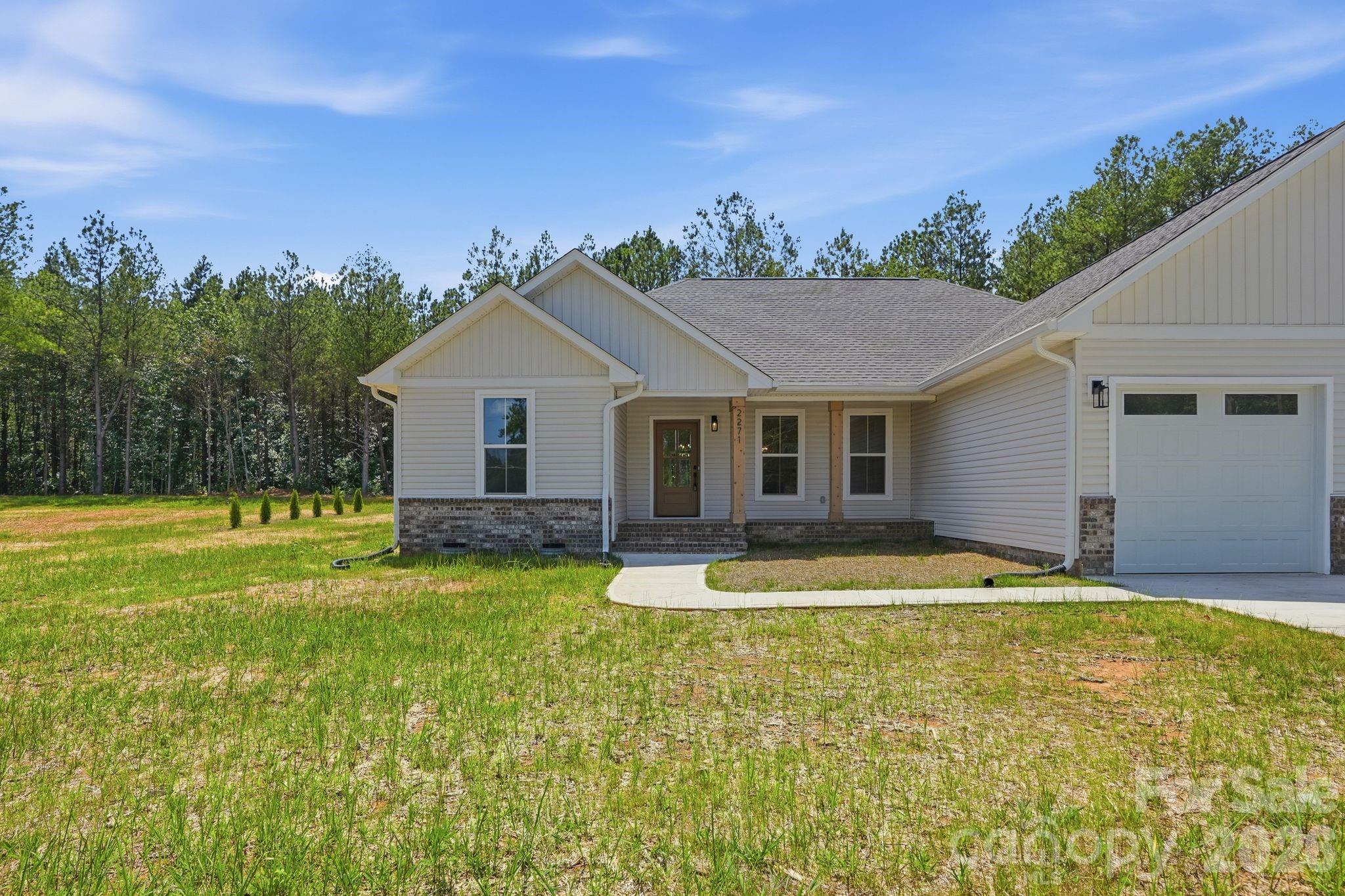 Recently completed and now available, welcome to North Pines—Lincolnton’s newest collection of thoughtfully crafted single-level homes by Brancer Homes. 2271 Lee Lawing Road blends elevated finishes, modern farmhouse charm, and the natural privacy of tree-lined homesites—all just 15 minutes from downtown Lincolnton and convenient to everyday shopping in Sherrills Ford and Denver.

The inviting exterior showcases classic brick accents and stained wood front-porch columns, delivering warm curb appeal with a clean farmhouse aesthetic. Inside, the builder’s Modern Farmhouse Designer Package combines crisp cabinetry finishes, curated lighting selections, stylish hardware, and quartz countertops throughout for a fresh yet timeless feel.

The open-concept kitchen features a spacious island with pendant lighting and flows seamlessly into the vaulted main living area, creating an airy, light-filled space ideal for both entertaining and daily living. The primary suite highlights a beautifully tiled shower wall and designer finishes that balance comfort with farmhouse-inspired character.

Additional features include added recessed lighting, a functional drop zone, and a well-appointed laundry room with upper cabinetry and quartz counters for enhanced storage and convenience. An extended two-car garage with exterior exit door, along with additional driveway parking, adds to the home’s everyday functionality.

Now that construction is complete, this home is part of a newly released collection in North Pines—offering a rare opportunity to own move-in ready new construction with elevated design and modern farmhouse appeal in one of Lincolnton’s fastest-growing areas.Additional features include added recessed lighting, a drop zone, and a laundry room with upper cabinets and quartz counter for extra storage and functionality. The home also includes an extended two-car garage with exterior exit door and additional driveway parking, making this layout as practical as it is stylish.

Set in a low-maintenance community with peaceful rural surroundings, this home pairs craftsmanship, modern design, and timeless farmhouse appeal—perfectly suited for life in Lincolnton.
