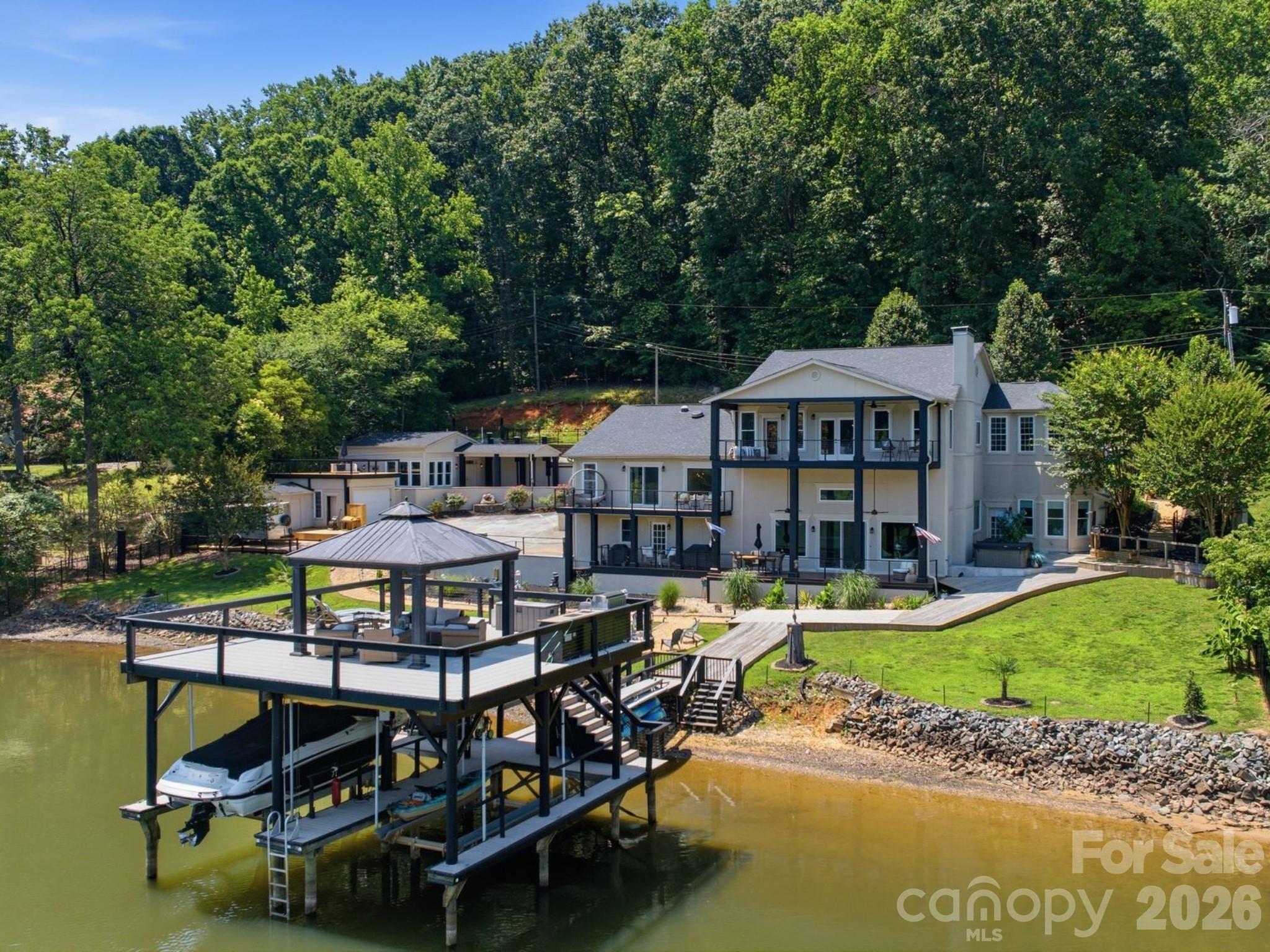 Nestled on a quiet cove of Lake Wylie and free from HOA restrictions, this exceptional gated waterfront home offers the perfect blend of luxury, privacy, and convenience, just a short commute from Charlotte. Thoughtfully designed for both entertaining and everyday lake living, the home showcases breathtaking year-round water views from multiple decks, covered patios, and a rare two-story dock with a grandfathered double boat lift that cannot be replicated today. The meticulously landscaped grounds and extensive renovations create an inviting atmosphere from the moment you arrive. This home is a life-style. The main level features an open-concept floor plan with panoramic lake views, abundant natural light, a chef's kitchen with stainless steel appliances, and a secondary primary suite ideal for guests, in-laws, or multi-generational living. The views from this luxury ensuite bedroom are simply spectacular.  The mid-level is dedicated to relaxation and entertainment, offering a media room with reclining theater seating for five, a wet bar, and an additional gathering space perfect for movie nights or unwinding after a day on the water. The luxurious primary suite serves as a private sanctuary, complete with a newly renovated spa-inspired bath featuring a soaking tub, a spacious walk-in closet, and a private balcony overlooking the lake, the perfect setting for morning coffee or sunset views.
The lower level provides remarkable flexibility with a second full kitchen, additional bedroom(s), a dedicated office, and easy access to outdoor living spaces. Just outside the office, an outdoor shower mirrors the elegant spa shower found inside, creating a resort-like experience. A hot tub overlooking the property offers the perfect place to relax and enjoy peaceful lake evenings. 
Adding to the home's uniqueness is an attached three-car garage, an additional detached garage, and a fully equipped fitness studio with its own private entrance, full bath, and kitchenette, ideal for a home gym, guest quarters, studio, or private workspace. The perfectly landscaped grounds also include a firepit with ample seating. Pea gravel walkway, trex decking, steel cable railing and a grilling station at the dock. 
This is a rare opportunity to own a truly distinctive Lake Wylie waterfront property that combines luxury, functionality, and an unmatched lake lifestyle.