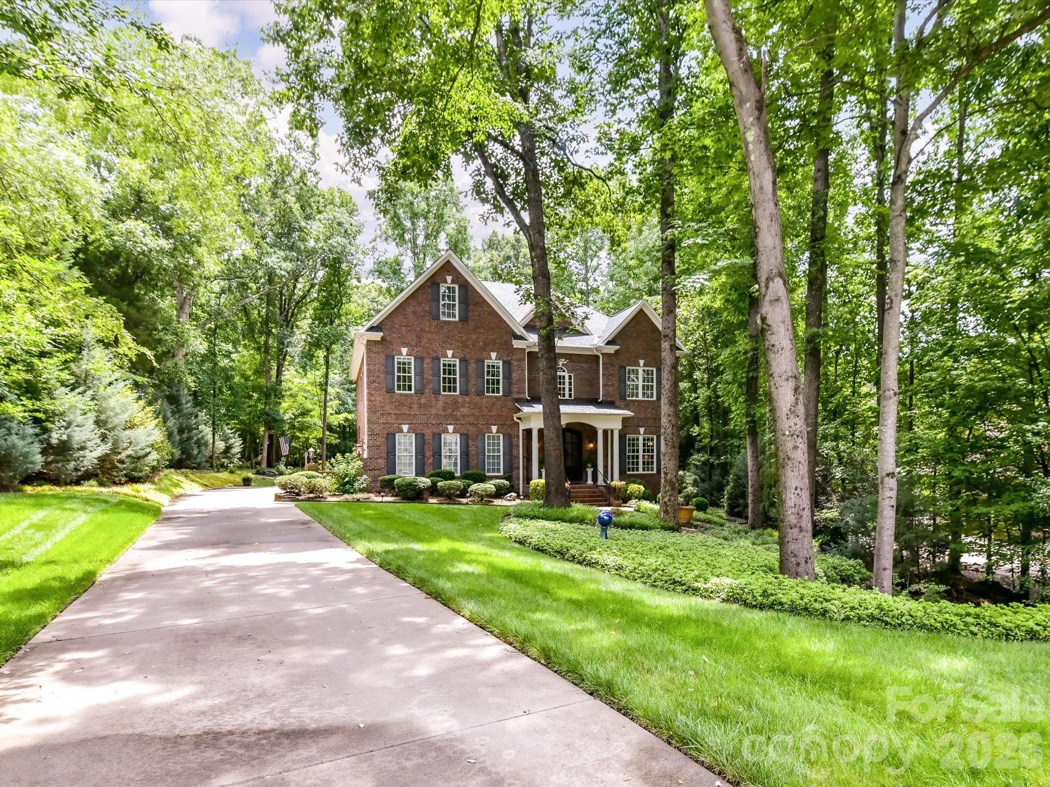 Tucked away on a beautifully wooded and private, 1+ acre lot, this custom brick home offers timeless elegance, exceptional living space, and thoughtfully designed indoor and outdoor entertaining areas across three finished levels. A dramatic two-story Great Room filled with natural light through massive windows, serves as the heart of the home, while the formal Dining Room and elegant sitting/flex room create the perfect setting for entertaining and everyday living. The spacious kitchen features abundant cherry cabinetry, generous prep space, and a sunny breakfast area overlooking the peaceful backyard retreat. The luxurious main-level primary suite offers a private escape complete with a spa-inspired bath featuring dual vanities, granite countertops, an oversized tiled walk-in shower, and adjoining flex space ideal for a home office, reading room, nursery, or exercise area. Spacious secondary bedrooms provide comfort and privacy, including ensuite bath access and large windows with serene wooded views. Upstairs, a stunning third-floor bonus retreat offers endless versatility with expansive recreation and media space, wet bar area, full bath, and additional flex rooms perfect for guests, hobbies, or multi-generational living. Rich hardwood floors, soaring ceilings, extensive crown molding, and custom architectural details add warmth and sophistication throughout the home. Outdoor living is equally impressive with a screened porch, covered deck with retractable awning, and professionally landscaped backyard featuring lush gardens, mature trees, and exceptional privacy. Gorgeous aerial views showcase the home’s tranquil setting and spacious wooded surroundings, creating a true retreat while still conveniently located near shopping, dining, and everyday amenities.