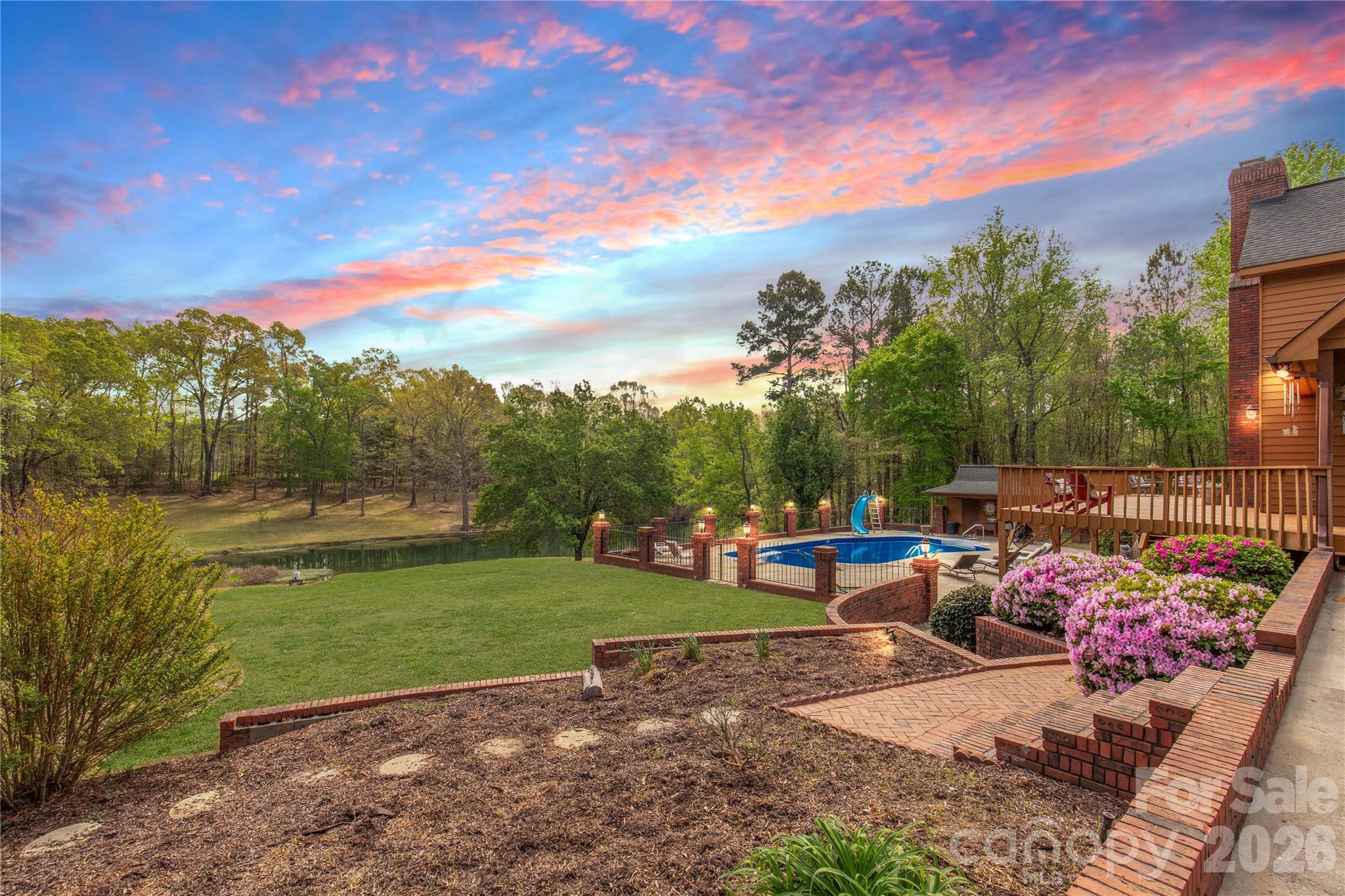 Welcome to a truly rare luxury estate set on over 3 acres, offering more than 5,600 heated square feet designed for those who crave space, privacy, and a resort-style lifestyle. Ideally located just minutes from Charlotte, this exceptional property offers the perfect balance of convenience and seclusion, creating a true private retreat.

Tucked into a peaceful setting, this custom wood-sided home makes an unforgettable first impression with its long driveway, manicured grounds, and inviting wraparound front porch—the perfect place to slow down and take in the surroundings, where it’s not uncommon to spot wild turkeys wandering through the backyard.

Inside, the home opens to a stunning two-story great room anchored by a statement fireplace and framed by double French doors that lead to an expansive back deck. From here, the view unfolds into a private outdoor oasis featuring a sparkling in-ground pool with a diving board and slide, along with a stocked pond that enhances the serene, getaway-like atmosphere.

The main level is thoughtfully designed for both comfort and flexibility, featuring a spacious primary suite that sets a new standard for relaxation with its spa-like bath, complete with a soaking tub, dual granite vanities, built-ins, a large walk-in ceramic shower, and the added luxury of two walk-in closets. The main floor also includes a well-appointed kitchen and a flexible bedroom or office space, making it ideal for remote work or guests.

Upstairs, two additional bedrooms, a full bath, and a loft overlook the pool and pond, creating a picturesque setting for a second living area, reading nook, or media space.

The walk-out basement is perfectly suited for extended living or entertaining, offering an expansive recreation room with built-in trophy and display cases, a wet bar, billiards area, fireplace, half bath, and a dedicated workout room. With direct access to the pool deck, this level provides excellent potential for multi-generational living, guest quarters, or a private retreat within the home.

Outdoors, the property continues to impress with a large back deck, a beautifully maintained fenced yard, and carefully curated landscaping accented by brick columns, hardscaping, and wrought iron details. Additional structures include a pool house, a four-bay detached garage, and dog kennels, providing both functionality and flexibility for a variety of lifestyles.

With walk-in attics, custom built-ins throughout, and every detail designed with intention, this home offers the perfect blend of luxury, space, and versatility. For those seeking a private estate with acreage, a pool, a pond, and room to accommodate multi-generational living—all within minutes of Charlotte—this is a rare opportunity to own a property that truly feels like a destination.