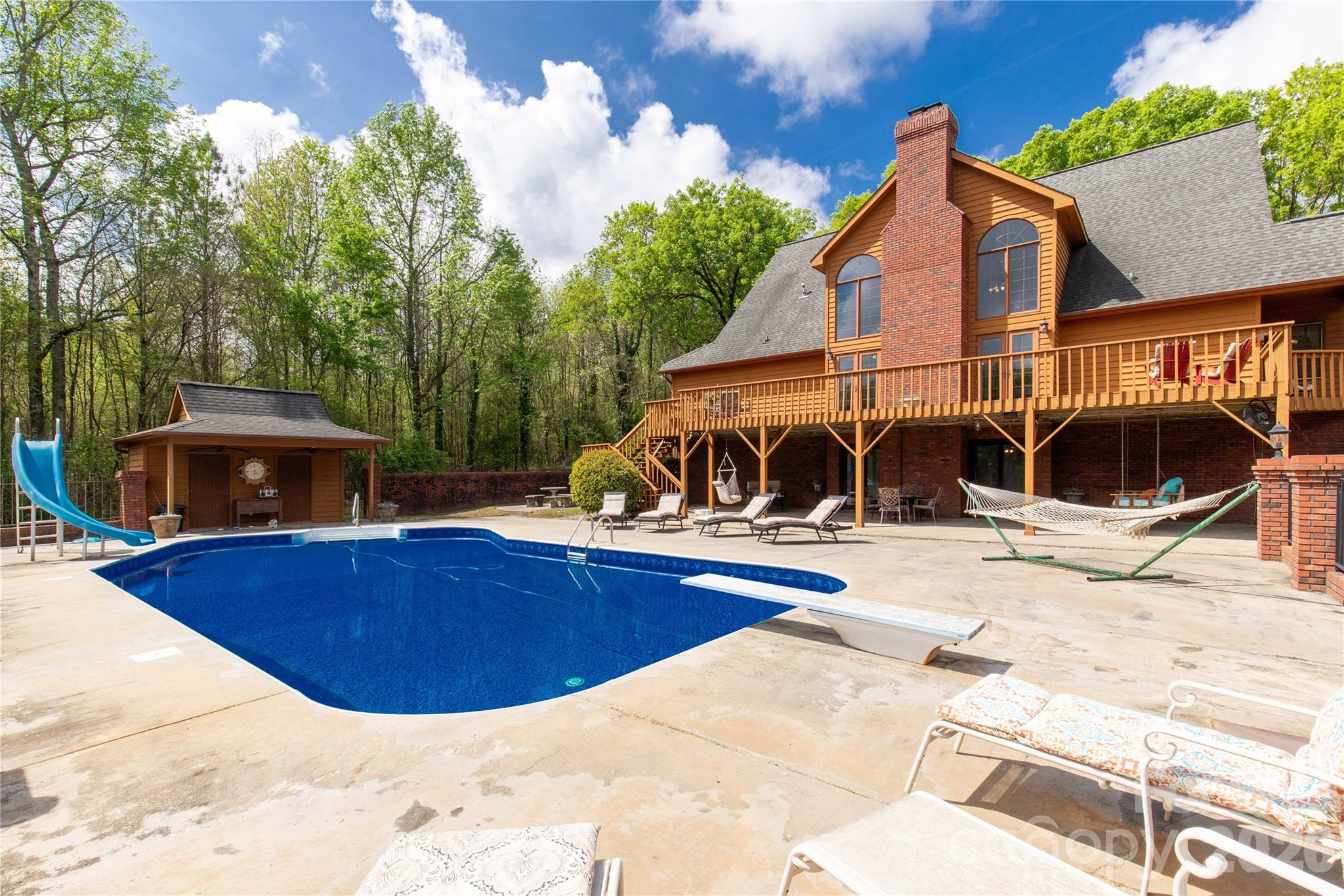 Welcome to a truly rare luxury estate set on over 3 acres, offering more than 5,600 heated square feet designed for those who crave space, privacy, and a resort-style lifestyle. Ideally located just minutes from Charlotte, this exceptional property offers the perfect balance of convenience and seclusion, creating a true private retreat.

Tucked into a peaceful setting, this custom wood-sided home makes an unforgettable first impression with its long driveway, manicured grounds, and inviting wraparound front porch—the perfect place to slow down and take in the surroundings, where it’s not uncommon to spot wild turkeys wandering through the backyard.

Inside, the home opens to a stunning two-story great room anchored by a statement fireplace and framed by double French doors that lead to an expansive back deck. From here, the view unfolds into a private outdoor oasis featuring a sparkling in-ground pool with a diving board and slide, along with a stocked pond that enhances the serene, getaway-like atmosphere.

The main level is thoughtfully designed for both comfort and flexibility, featuring a spacious primary suite that sets a new standard for relaxation with its spa-like bath, complete with a soaking tub, dual granite vanities, built-ins, a large walk-in ceramic shower, and the added luxury of two walk-in closets. The main floor also includes a well-appointed kitchen and a flexible bedroom or office space, making it ideal for remote work or guests.

Upstairs, two additional bedrooms, a full bath, and a loft overlook the pool and pond, creating a picturesque setting for a second living area, reading nook, or media space.

The walk-out basement is perfectly suited for extended living or entertaining, offering an expansive recreation room with built-in trophy and display cases, a wet bar, billiards area, fireplace, half bath, and a dedicated workout room. With direct access to the pool deck, this level provides excellent potential for multi-generational living, guest quarters, or a private retreat within the home.

Outdoors, the property continues to impress with a large back deck, a beautifully maintained fenced yard, and carefully curated landscaping accented by brick columns, hardscaping, and wrought iron details. Additional structures include a pool house, a four-bay detached garage, and dog kennels, providing both functionality and flexibility for a variety of lifestyles.

With walk-in attics, custom built-ins throughout, and every detail designed with intention, this home offers the perfect blend of luxury, space, and versatility. For those seeking a private estate with acreage, a pool, a pond, and room to accommodate multi-generational living—all within minutes of Charlotte—this is a rare opportunity to own a property that truly feels like a destination.