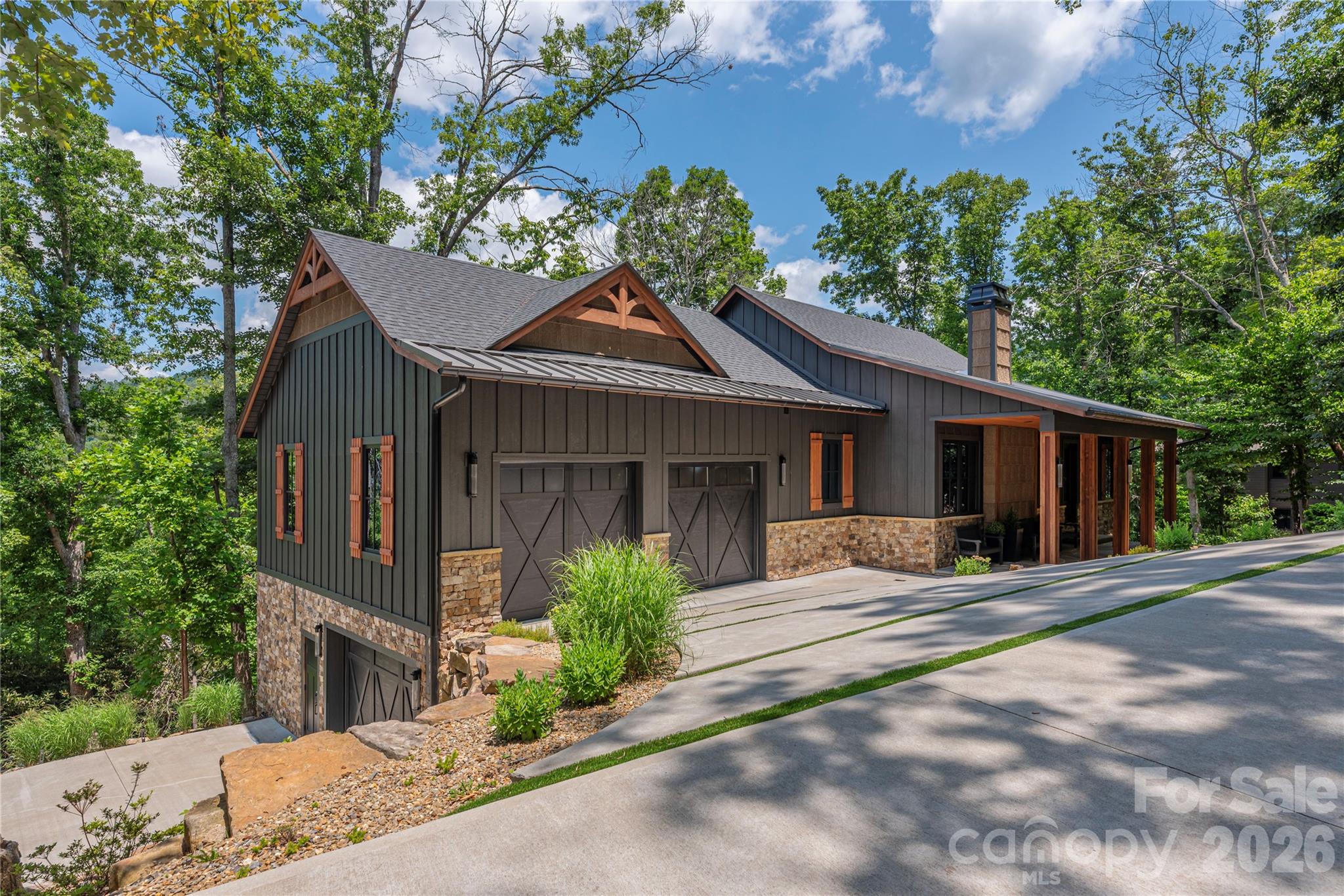 Discover the perfect blend of modern luxury and peaceful mountain living in this custom-designed contemporary farmhouse, ideally nestled in nature with serene mountain views. Designed for both everyday living and effortless entertaining, the open-concept main level features a stunning great room anchored by a cozy gas log fireplace that seamlessly connects the living and dining spaces. The chef-inspired kitchen is equally impressive, showcasing a large center island, sleek glass cooktop with designer accent hood, built-in oven, microwave, and convenient dishwasher drawers for easy cleanup. Step outside through expansive sliding glass doors to the covered back deck where a linear gas firepit creates the perfect setting to relax and enjoy the views in every season. Beautiful sunrises and sunsets  peak through the trees adding to the experience. A built-in gas grill makes outdoor dining and entertaining a delight. Back inside the home a luxurious primary suite offers a true spa experience, complete with a beautifully appointed bath featuring floor-to-ceiling tile, heated floors, and a barrier-free walk-in shower. Practicality meets style with a spacious mudroom/laundry area conveniently located just inside the garage entrance, providing the perfect drop zone for everyday life. The walk-out lower level expands your living space with a welcoming family room, two additional bedrooms, a dedicated office, a second laundry room, and a spacious workshop garage ideal for hobbies, projects, or extra storage. Fitness enthusiasts will appreciate the private home gym, which may be included with the sale and comes equipped with its TV and exercise equipment. Built with exceptional comfort and efficiency in mind, this home features a whole house generator, geothermal heating and cooling, radiant heated floors throughout the entire lower level, a tankless water heater, triple-pane windows and a central vacuum system. End your day gathered around the outdoor firepit, where there's plenty of room for s'mores, conversation, and creating lasting memories under the stars. This exceptional property offers the rare opportunity to enjoy refined living surrounded by the beauty and tranquility of the mountains.