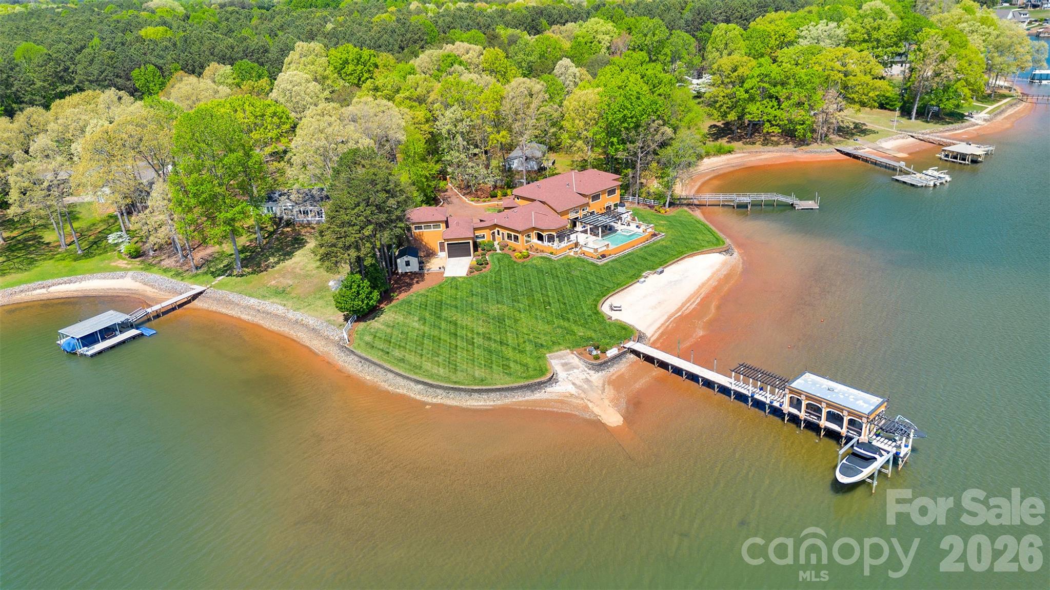 A truly rare offering on Lake Norman, this extraordinary Mediterranean-inspired waterfront estate is privately positioned behind gates on nearly an acre, showcasing approximately 500 linear feet of shoreline and a natural sandy beach—an exceptional combination that creates both dramatic presence and effortless lakefront living.
Designed to capture breathtaking sunrise-to-sunset panoramic water views, the residence blends timeless architecture with resort-style amenities and remarkable privacy. Expansive terraces and outdoor entertaining areas create a seamless connection between elegant interiors and the beauty of the lake beyond.
At the heart of the home, the oversized gourmet kitchen featuring three sinks is thoughtfully designed for both everyday living and large-scale entertaining, offering generous workspace and effortless flow into the main gathering spaces. Each bedroom is appointed with its own private ensuite bath, creating a true retreat experience for both residents and guests. Elevator shaft in place for future elevator. Adding exceptional flexibility, the property also features a private studio apartment located above the oversized garage and RV bay, complete with its own full kitchen and washer/dryer hookup—ideal for extended family, visiting guests, multigenerational living, or a private executive-style workspace with separation from the main residence. Outdoor living reaches another level at the private pier, which serves as its own lakeside entertaining destination, complete with a built-in dockside kitchen featuring a sink, BBQ, griddle, refrigerator, and ice maker. Two boat lifts provide convenient access for multiple watercraft, making spontaneous days on the lake beautifully effortless. Collectors and adventure enthusiasts will appreciate the oversized garage with a dedicated third-bay RV garage, offering exceptional space for vehicles, boats, and recreational equipment.
Set behind a private gated entrance with no HOA restrictions, this estate offers a rare combination of privacy, flexibility, and shoreline scale that is increasingly difficult to find on Lake Norman. The expansive waterfront setting, sandy beach frontage, and sweeping views create an unforgettable sense of arrival and a lifestyle defined by both elegance and recreation. From sunset gatherings along the shoreline to mornings launching directly from your private pier, every element of this residence reflects intentional design and effortless luxury. With remarkable shoreline presence, Mediterranean architectural character, dual boat lifts, a fully equipped dockside kitchen, private guest quarters above the RV garage, ensuite accommodations throughout, and unmatched privacy, this exceptional Sherrills Ford waterfront estate represents a rare opportunity to own a true Lake Norman legacy property.