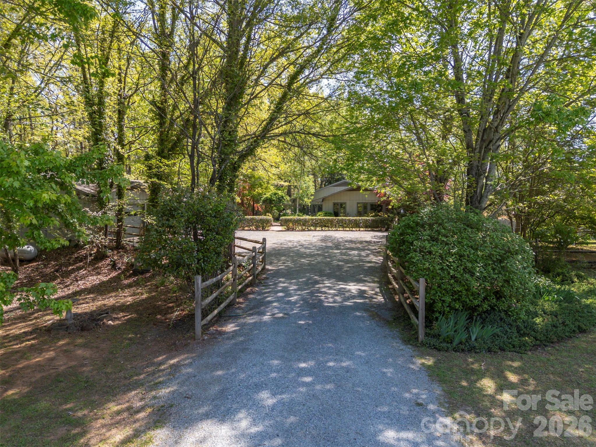 Tucked along a private drive in the sought-after Hunting Wood community, this Tryon retreat on 9.6 acres offers the rare combination of extensive, one-level living space, privacy, and “lifestyle” amenities. The main residence features 3,125 heated sq ft with 8 natural light-filled rooms, 4 bedrooms, and 3.5 baths, plus a 603 sq ft finished basement. Enjoy cozy evenings by the fireplace, then step outside to a property designed for everyday living and effortless entertaining. The grounds are a woodland retreat: brick walkways, a vine-draped arbor, wooded garden paths, and a tranquil water garden/pond create a peaceful, storybook setting. Out back, there's a large covered porch with a hot tub and a fenced yard for the dogs. Summer becomes a staycation with the in-ground swimming pool and expansive pool deck—perfect for gatherings, lounging, and outdoor dining. For hobbyists and creatives, the property shines with a detached garage with separate dedicated wood shop, a small greenhouse, and an additional artist studio—a true compound for work, play, and inspiration.
Move-in with confidence: the sellers completed a pre-inspection and proactively addressed the maintenance items identified—delivering a home that feels cared for from top to bottom. In addition to a list of minor items addressed, major improvements include a new roof and crawl space encapsulation. If you’re looking for a home that offers privacy, character, and resort-style amenities—plus the peace of mind of thorough proactive maintenance—this is a must-see.