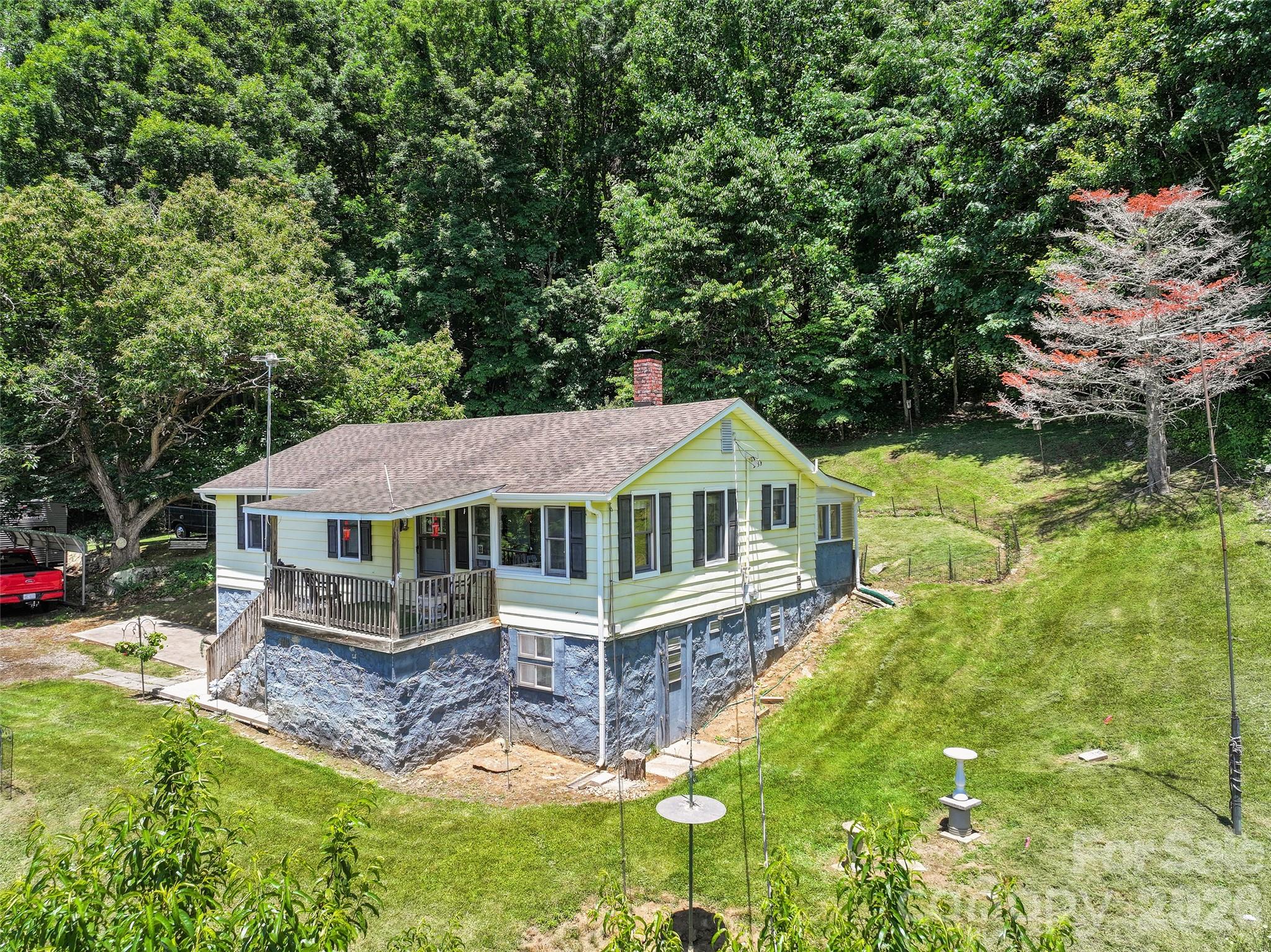 Situated in the heart of the Western North Carolina mountains, this traditional-style home offers 960 square feet of comfortable living space with long-range mountain views from the covered front porch. Perfect for those seeking peaceful back to simple country living, the property sits on 3.2+ acres along a well-maintained state road for easy year-round access. The home features three bedrooms and one full bath, a welcoming living room with cozy wood burning stove and a functional eat in kitchen area ideal for everyday living and casual gatherings. A separate unheated, closed-in rear porch provides additional flexible space, while a private rear patio is perfect for outdoor relaxation. Downstairs, you’ll find a large unfinished basement with a single-car garage and convenient laundry area. Outside, the property shines with a spacious outbuilding for storage or projects, plus a double freestanding carport equipped with RV hookup—ideal for visitors or hobbyists. Additional highlights include a private well and septic system, mature apple trees that add seasonal charm, and abundant outdoor space to enjoy the mountain lifestyle.