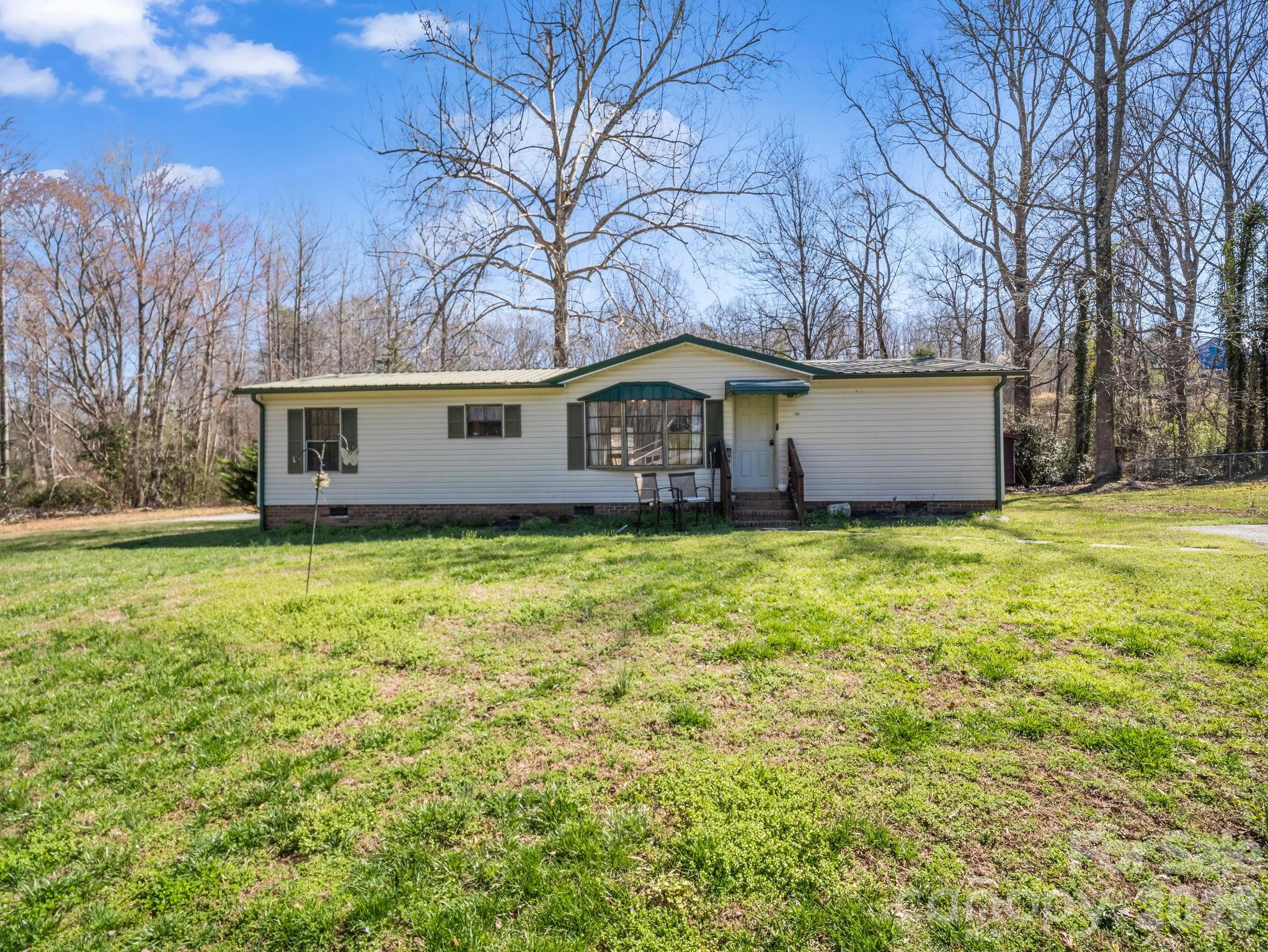 Enjoy peaceful small-town living in the charming Town of Landrum with this inviting doublewide home situated on almost half an acre. Nestled on a level corner lot with a gentle creek, this property offers both space and a tranquil setting while still being convenient to downtown Landrum’s shops, restaurants, and everyday amenities.
Inside, the home features 3 bedrooms and 2 full bathrooms with an open living and dining area highlighted by vaulted ceilings, creating a bright and spacious atmosphere. The spacious kitchen offers plenty of room for cooking and entertaining, making it the heart of the home for gatherings with family and friends. Step outside to enjoy the natural surroundings, where the creek provides a peaceful backdrop to the property. The generous yard offers space for gardening, outdoor activities, or simply relaxing in your own private setting. Two outbuildings provide excellent storage for tools, hobbies, or outdoor equipment. With a little TLC, this property presents a great opportunity for an affordable primary residence or investment property. Whether you’re looking to create your own comfortable home or add to your investment portfolio, this property offers potential in a desirable Landrum location.