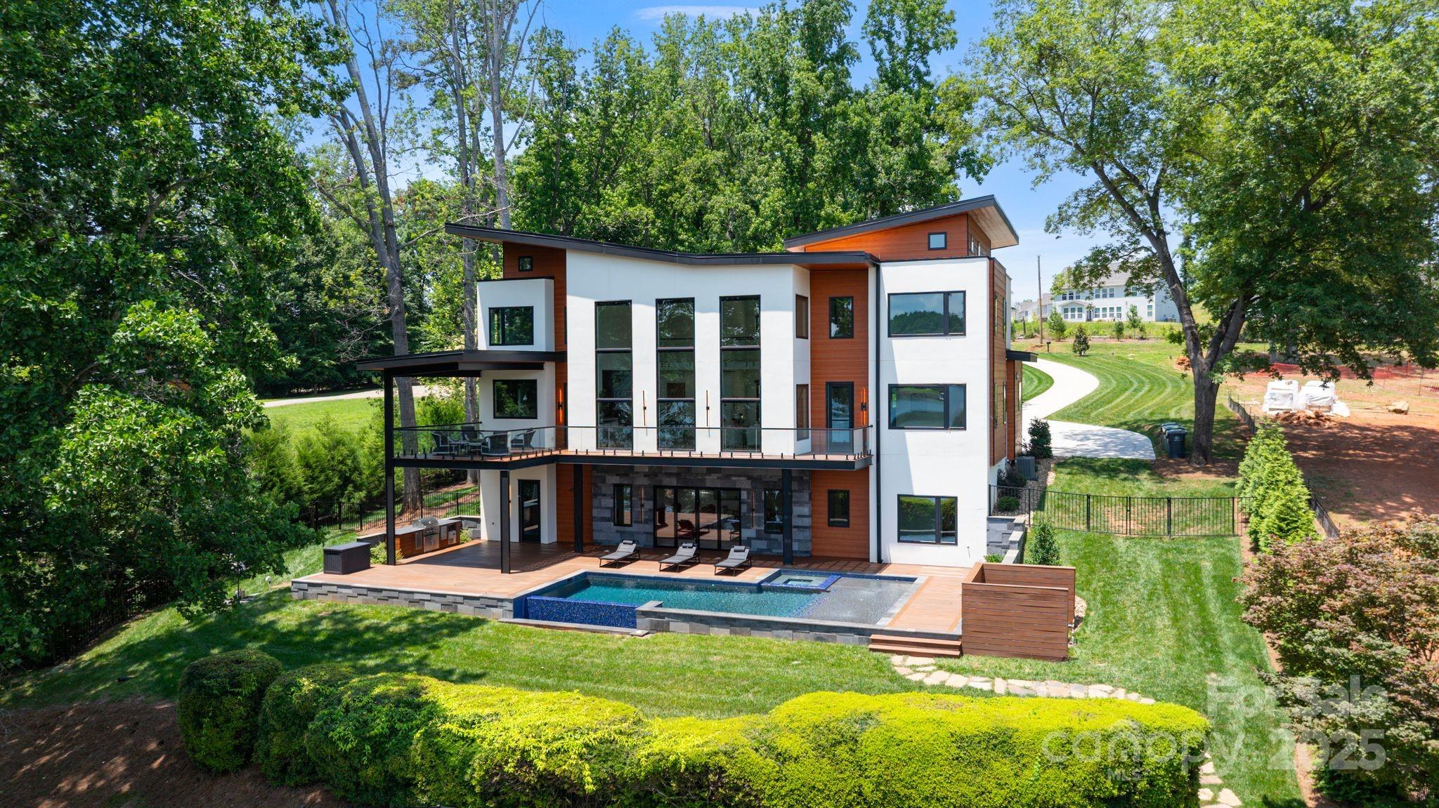 Experience lakefront luxury just 20 minutes from uptown Charlotte at 5930 Midsomer Road. This custom-built, four-bedroom, four-full-bath, two-half-bath home on Lake Wylie features high-end finishes, including smooth hard-coat stucco, Balinese lava stone, and exotic cumaru wood. Enter through an 8-foot glass door to soaring 22-foot ceilings and panoramic lake views. The open-concept living room features floor-to-ceiling windows and a striking stone fireplace. The chef’s kitchen offers Monogram appliances, a 10' waterfall island, and opens to a covered outdoor kitchen and patio. Main-level primary suite includes lake views, deck access, and a spa-like bath with wet room and freestanding tub. The walk-out basement includes a full bar, guest suite, and seamless access to the resort-style infinity pool, spa, and tanning ledge. Additional features: outdoor shower, built-in grill, and private dock with boat lift. This is lakeside living redefined!