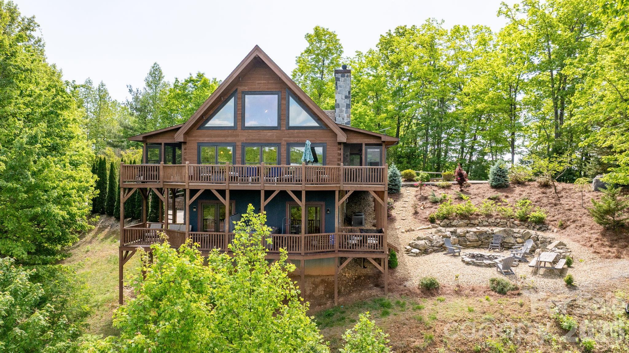 Perched high above the Blue Ridge landscape in the gated Timber Rock community, 6749 Fire Crest Lane captures the essence of refined mountain living. Set on 2.84 wooded acres at over 2,000 feet in elevation, this custom-built log retreat showcases breathtaking year-round views of Grandfather Mountain and the surrounding North Carolina mountains. Located just minutes from Blowing Rock, Boone, the Blue Ridge Parkway, hiking trails, skiing, shopping, and dining, the home offers both peaceful seclusion and convenient access to the best of the High Country. Inside, soaring cathedral ceilings, expansive windows, and rich wood interiors create a warm yet elevated atmosphere filled with natural light and multi-layered mountain views. At the center of the home, a stunning stone fireplace anchors the inviting living space, blending rustic character with timeless comfort. Designed for effortless everyday living and entertaining, the main level features a spacious primary suite, guest bedroom, open-concept kitchen with breakfast bar and pantry, generous dining area, powder bath, and laundry. Multiple decks and screened porches extend the living experience outdoors, creating unforgettable spaces for morning coffee, evening sunsets, and relaxing in the cool mountain air. Upstairs, a loft-style sitting area leads to a third bedroom suite with full bath and abundant storage. The finished lower level offers exceptional flexibility and is currently configured as an additional sleeping area with full bath, great for guests, recreation, or multi-generational living. Outdoor spaces are equally impressive, with a fire pit and picnic area designed for gathering beneath the stars, a semi-circular drive for easy arrival, and additional lower-level access to the oversized two-car garage. Offering approximately 2,763 heated square feet, the home combines authentic mountain architecture with modern comfort and quality craftsmanship throughout. Additional features include remote-controlled blinds, radon mitigation system, architectural shingle roofing and low-maintenance ownership within a peaceful gated setting. Furnishings are also included with few personal exceptions and with an acceptable offer and terms. Short-term rentals are permitted, making this property an exceptional opportunity as a luxury mountain residence, retreat, or income-producing investment. Residents of Timber Rock also enjoy access to the Owner’s Pavilion complete with gathering spaces, grilling areas, wood-burning fireplace, kitchen facilities, restrooms and scenic picnic areas along the Yadkin River & Jackson Camp Creek. With low annual HOA dues and an extraordinary setting that embodies the beauty of the Blue Ridge Mountains, 6749 Fire Crest Lane offers a rare opportunity to experience mountain living at its finest.