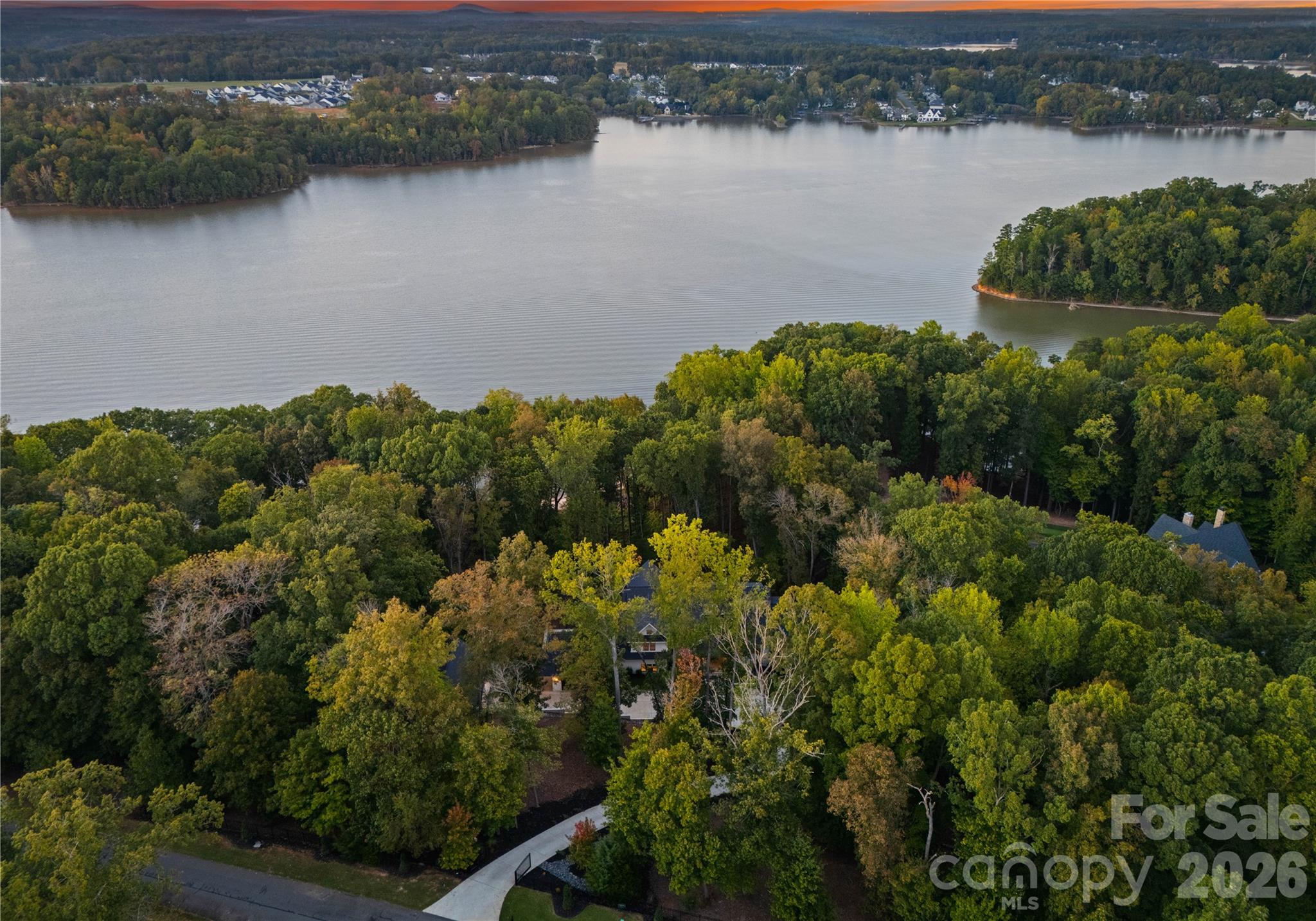 A private gate introduces this modern waterfront masterpiece in the prestigious Sanctuary community, where architecture, light, and water converge. A pivoting front door opens to a dramatic great room with 12’ ceilings, collapsing glass walls, French oak floors, and a linear gas fireplace—all framing panoramic wooded views of Lake Wylie.
The sculptural kitchen centers on an oversized waterfall island wrapped in backlit Crystalita stone and is equipped with professional-grade appliances: WOLF 6-burner range, True custom refrigeration, pellet ice maker, double-drawer dishwashers, and a fully appointed scullery with Miele coffee system.
The main-level owner’s suite is a private retreat with screened in porch, fireplace, illuminated boutique-style closets, and a spa bath featuring backlit stone, dual vanities, dual water closets, oversized dual-entry rain shower, and soaking tub. Upstairs are four generous bedrooms with ensuite and Jack-and-Jill configurations.
Flexible lifestyle spaces include a bonus room, theater-ready room, wellness/yoga room, exercise room, and wet-bar-ready studio. Dual laundry rooms and a quartzite drop zone with personal lockers add everyday ease.
Resort-style outdoor living showcases a heated saltwater pool, outdoor bath, in-ground trampoline, and covered lake-view balcony with IPE flooring, heaters, fans, and gas fireplace. Dock plans approved by Duke Energy & HOA available.
Garages include a two-car attached, a framed/plumbed/wired two-car detached with carriage house plans, plus a golf-cart garage in the basement. Smart home features: Lutron controls, Emtek hardware, Restoration Hardware lighting.
Community amenities: boat slip, tennis courts, pool, playground, fitness center and kayak storage for lease. Shopping, dining, airport, and Uptown Charlotte at your fingertips. A residence designed not just to live in—but to experience.

For more information regarding the community, visit: https://thesanctuaryatlakewylie.com/living-at-the-sanctuary/