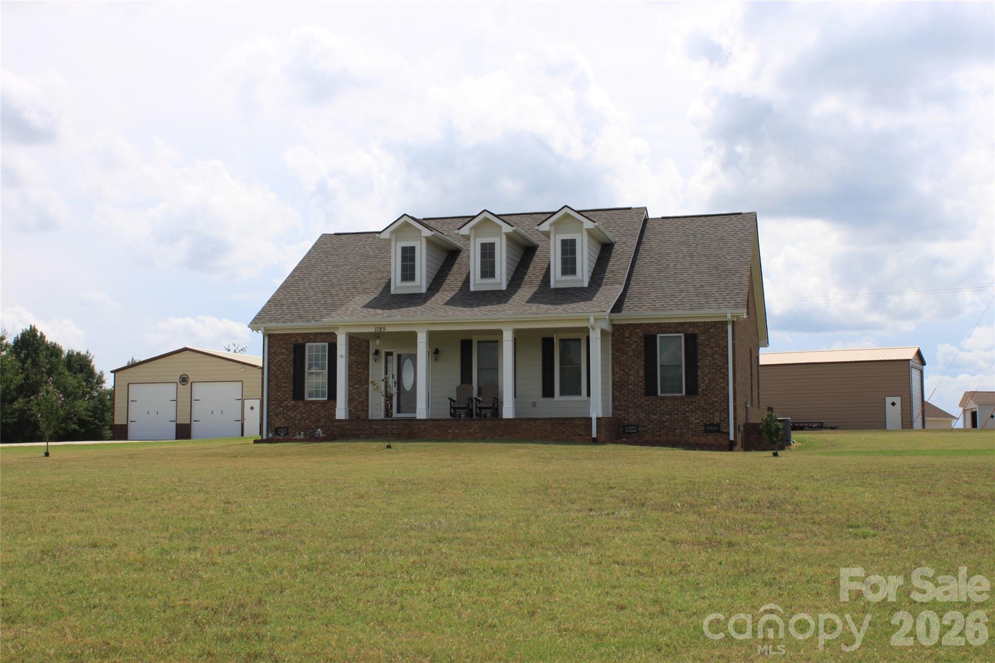 Set on 2.8 acres, this 3 bed, 2.5 bath Cape Cod offers 2,612 sq. ft. of thoughtfully designed living space with a welcoming blend of comfort, privacy, and flexibility. The main level features an open layout that connects the living, dining, and kitchen areas, creating an inviting setting for everyday living and entertaining. Hardwood floors, abundant natural light, and a gas log fireplace add warmth and character, while the kitchen is finished with granite counters, stainless appliances, a breakfast bar, and generous cabinetry. All 3 bedrooms are conveniently located on the main level, including a spacious primary suite with a large bath featuring dual vanities, a soaking tub, and separate shower. Upstairs, an expansive finished bonus area with a half bath provides excellent options for a rec-room, office, studio, extra bedrooms or additional flex space. Covered front and rear porches extend the living areas outdoors. Home has an attached 2-car garage, a detached 30x30x12 garage w/2 electric doors and entrance door, and a 18x51x14 building with one 14x14 door and one entrance door. With a level setting, no HOA dues, and easy access to nearby shopping and entertainment, this property offers room to relax, work, and enjoy a more peaceful pace of life.