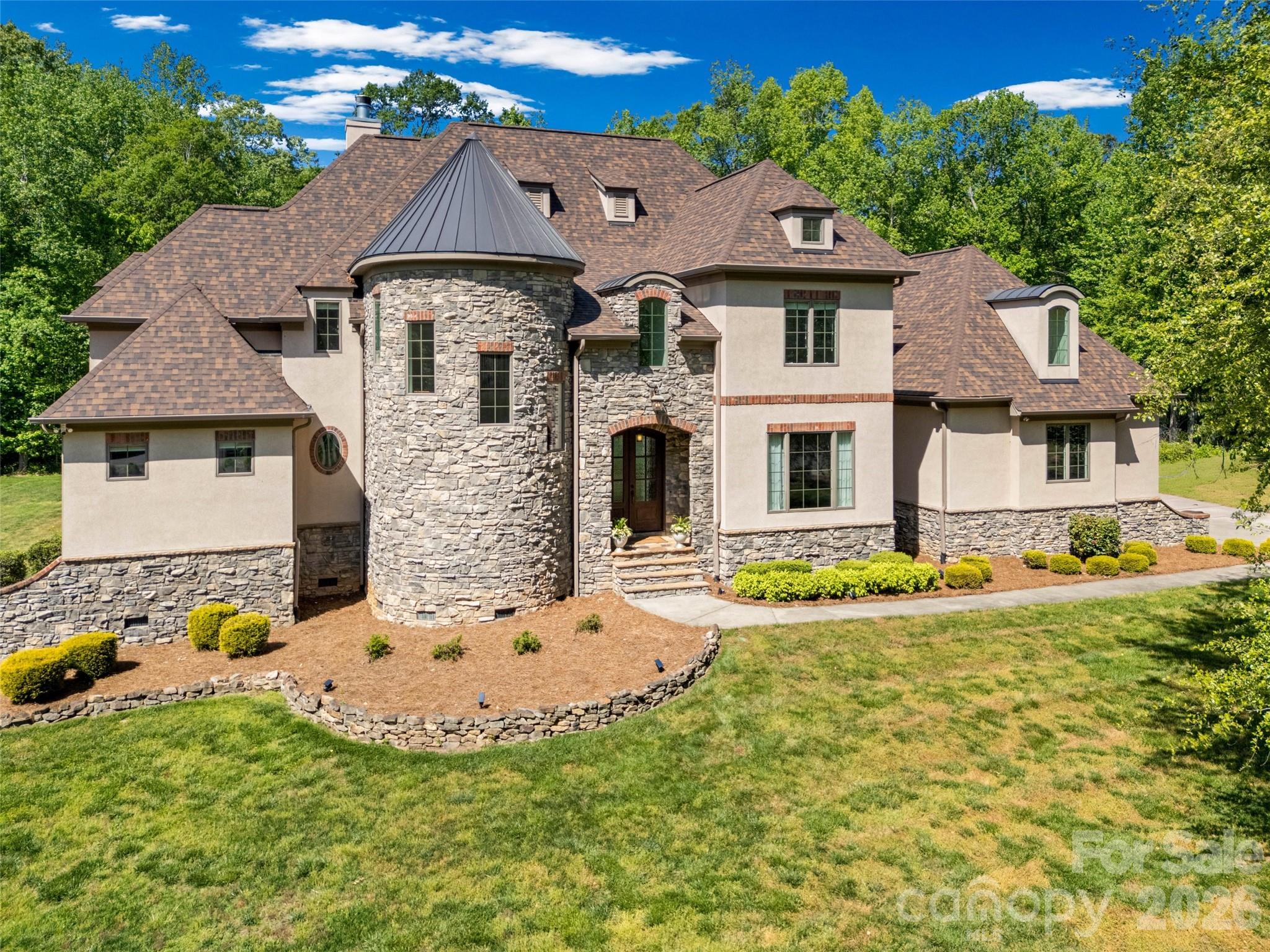 Discover unparalleled luxury and privacy in this stunning custom-built French Chateau-style estate, situated on a private, wooded 2.28-acre cul-de-sac lot within the exclusive gated community of Stillwell. This 2013-built home offers 5,521 square feet of refined living space with 5 bedrooms, 4 full bathrooms, and 2 half baths. The dramatic circular turret, extensive stonework, and elegant European-inspired architecture create an immediate sense of grandeur from the moment you arrive. Inside, a grand foyer with soaring ceilings and a sweeping circular staircase welcomes you into an open-concept floor plan designed for both sophisticated entertaining and comfortable family living. Highlights include a chef’s kitchen with breakfast area, expansive great room, luxurious main-level primary retreat, private office, formal dining room, and multiple ensuite bedrooms. High-end finishes such as tray and coffered ceilings, built-ins, and abundant natural light elevate every space. Outside, the resort-style in-ground saltwater pool with creates the ultimate private oasis for year-round entertaining, all surrounded by expansive wooded grounds that offer exceptional privacy and tranquility. The oversized 4-car garage provides ample space with the potential to add additional structures such as a workshop, guest house, or carriage house. Nestled in the prestigious Stillwell community this home offers a peaceful countryside lifestyle while remaining conveniently close to Birkdale Village for upscale shopping and dining. Just minutes from Lake Norman, Latta Plantation, and Charlotte’s major employment centers, this property perfectly balances exclusivity, privacy, and accessibility. This is a rare opportunity to own a true custom luxury estate that celebrates timeless elegance, privacy, and an extraordinary lifestyle on one of the most desirable lots in the community. Schedule your private showing today.