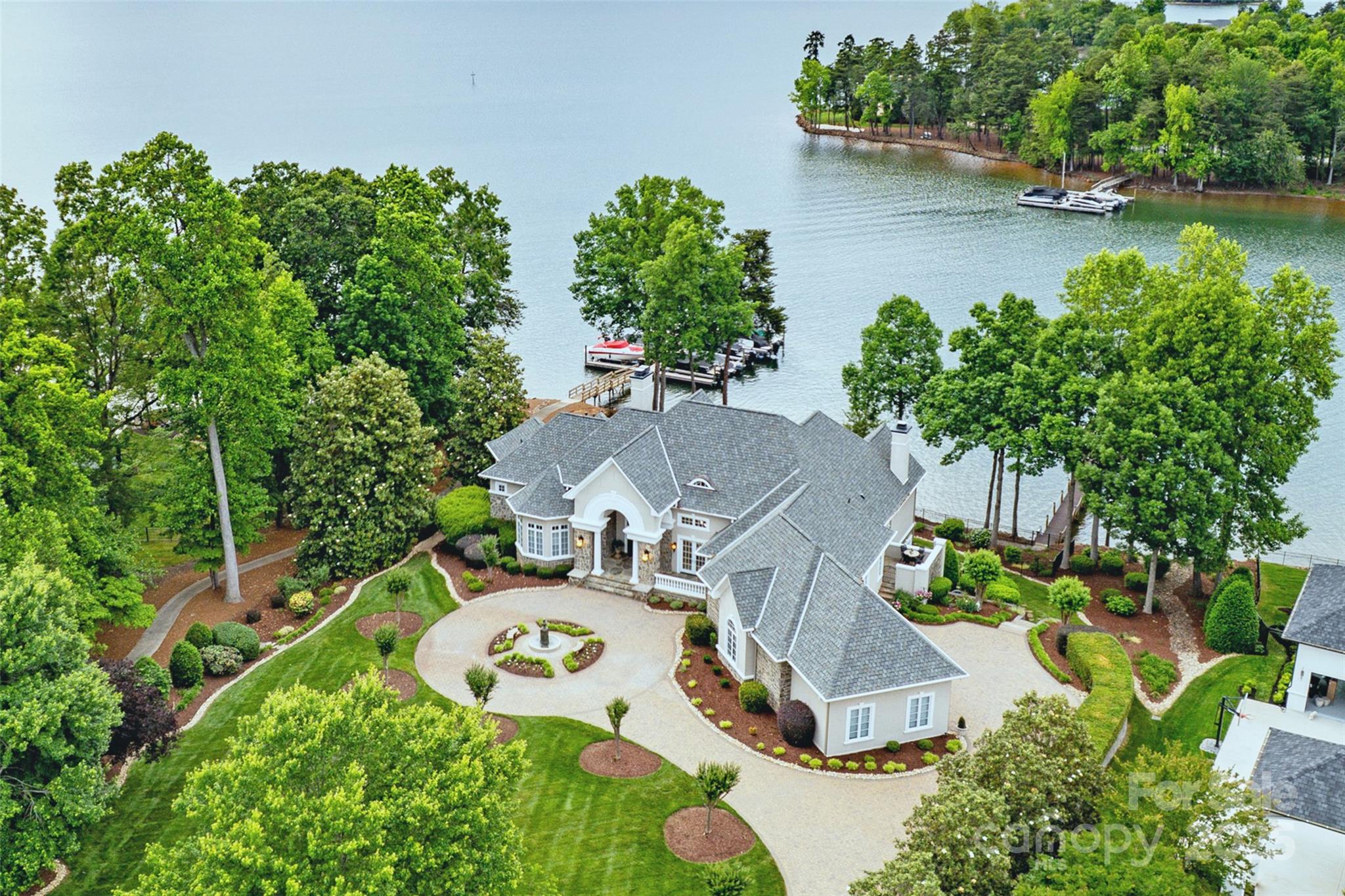 This extraordinary lakefront residence artfully combines timeless architecture with refined living—all set against the breathtaking backdrop of Lake Norman. Nearly every room captures sweeping 5-mile water views across the lake and magnificent summer sunsets, while the outdoor oasis invites both relaxation and entertaining with a saltwater pool, spa, waterfall, outdoor kitchen, fire pit, multiple patios and balconies, and a private dock with boat and PWC lifts. Inside, the main level showcases clean lines, soaring ceilings, and casual elegance. The gathering spaces include a gourmet kitchen with keeping room and premium stainless appliances. The magnificent primary suite features a spa-style bath with heated floors, steam shower, and dual walk-in closets, complemented by a private guest suite and beautifully designed living areas. The lake level is perfect for entertaining, offering two ensuite bedrooms, a spacious family room, full bar with wine cellar, media and billiard rooms, golf simulator, fitness area, game room, full bath, and a versatile flex/storage space with a second laundry. Pristine in condition and maintained with meticulous care, this home reflects exceptional craftsmanship and attention to detail throughout, highlighted by exquisite finishes, custom paintwork, and marble and quartz surfaces. A brick-toned tumbled paver circular drive and elegant fountain create a grand first impression, while the wide, deep-water cove offers tranquil views of the TNGCC golf course.