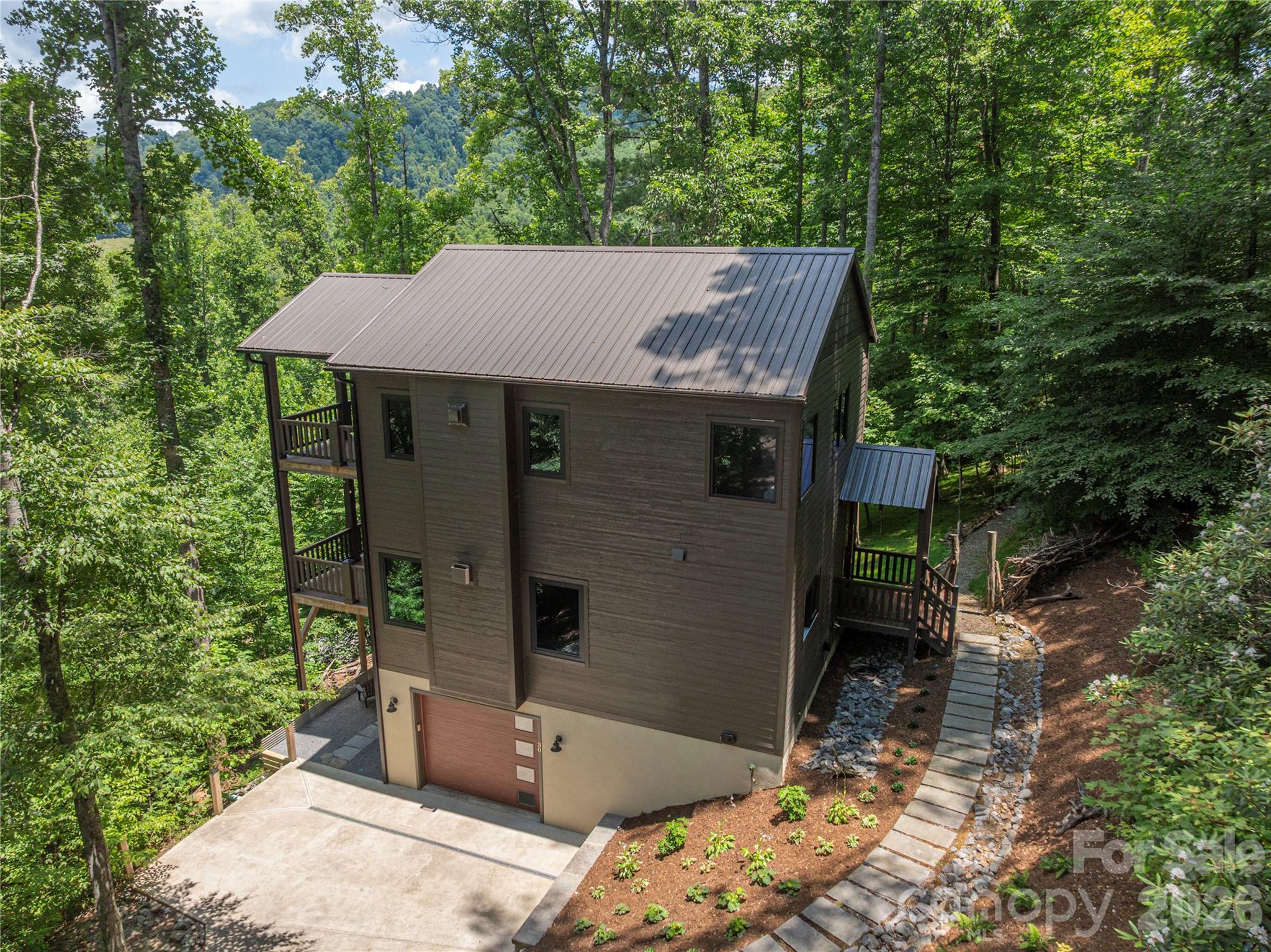Escape to your own private mountain retreat in this custom-designed contemporary home, where modern comfort meets the tranquility of nature. Thoughtfully crafted with exceptional attention to detail, this two-bedroom home offers the perfect blend of style, functionality, and privacy—ideal as a full-time residence, weekend getaway, or potential income-producing rental. The inviting main level features a bright, open-concept floor plan designed for effortless living and entertaining. At the heart of the home is a beautifully appointed kitchen with granite countertops, a large center island, and abundant workspace, flowing seamlessly into the spacious living area anchored by a cozy gas fireplace. Expansive sliding glass doors open to a generous back deck, creating an ideal setting for outdoor dining, entertaining guests, or simply relaxing while taking in the peaceful sounds of nature. A convenient half bath completes the main level. Upstairs, you'll find two bedrooms and two full bathrooms, including a luxurious primary suite designed to feel like a private spa. Enjoy heated tile floors, an elegant walk-in shower with floor-to-ceiling tile and natural riverstone accents–the perfect peaceful atmosphere for unwinding after a day of adventure. The second bedroom is just steps from a beautifully finished full bath, while the upstairs landing area is the perfect space for a reading nook, home office, or cozy sitting area. The lower level adds exceptional functionality with a spacious laundry room offering abundant storage, and the basement garage includes a convenient pet-wash station—perfect after hiking the nearby trails or exploring the outdoors with your four-legged companions. Throughout the home, thoughtful upgrades such as heated tile floors, granite countertops, oversized transom windows that fill the interior with natural light, and quality craftsmanship create a warm yet sophisticated mountain escape. Just a short stroll from the home, a private patio offers s’more outdoor space with a firepit to enjoy under the stars. Whether you're searching for a peaceful primary residence, a lock-and-leave second home, or a potential vacation rental, this exceptional mountain retreat offers the perfect balance of luxury, comfort, and natural beauty.