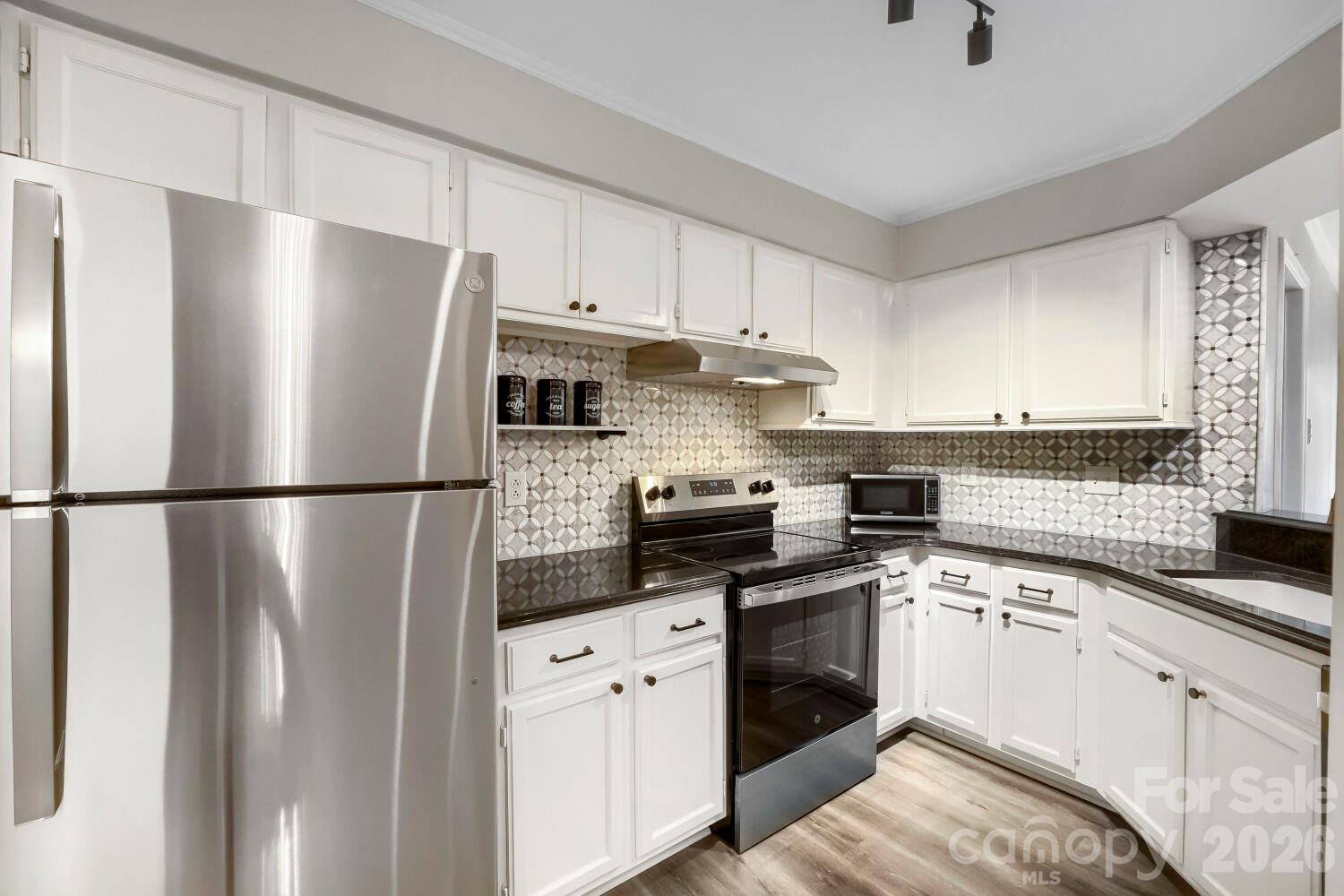 Picture your Saturday morning. You step out onto your private patio, coffee in hand, and look out over a glassy community pool just steps from your door. Ducks glide across the pond with a sparkling fountain on your daily walk. The amenities feel more like a vacation property than a condo complex. Just across the street, Quail Corners Shopping Center has you covered with Harris Teeter, Walgreens, a cocktail bar, restaurants, and your daily Starbucks run — and a quick five-minute drive lands you in the middle of SouthPark, with its premier shopping, fine dining, and entertainment all within reach. You get the South Park lifestyle and address without the South Park price tag.
Walk through the front door and you immediately notice the difference. This isn't a "needs work" condo — it's been freshly painted from top to bottom, with updated kitchen and bathrooms, sleek laminate wood flooring throughout, and updated black door hardware and light fixtures that give every room a polished, current feel.
The kitchen has been thoughtfully refreshed with on-trend tile backsplash, a deep farmhouse-style sink, sleek black fixtures, and gold hardware accents that pop against crisp white cabinetry. Stainless steel appliances complete the look. It opens effortlessly to the dining area, which carries the same laminate wood flooring, crown molding, and a decorative overhead light — making it easy to imagine dinner parties that spill from the kitchen counter to the table without missing a beat.
From the dining area, you flow right into the great room — the true heart of this home. A wood-burning fireplace with a rustic wood mantel anchors the space, while a statement fandelier overhead ties the room together. Triple glass doors lead out to your private patio with views of the community pool, blurring the line between indoor comfort and resort-style outdoor living. This is where morning coffee turns into evening wine, where a good book on a rainy day feels like a retreat.
The primary bedroom offers the same warm laminate flooring and its own set of double glass doors opening to the patio and pool view — because why should the great room have all the fun? A large walk-in closet provides the storage downsizers and first-time buyers alike are looking for, and the ensuite bath delivers a true spa moment: tile flooring, a decorative accent tile wall, a glass shower, matte black fixtures, and a custom wood vanity with a farmhouse sink that feels straight out of a design magazine.
Bedroom #2, situated at the front of the home, offers a double-door closet and its own private entry into Bath #2 — ideal for guests, a roommate, or a dedicated home office. That second bath brings its own charm with tile flooring, a tiled tub/shower combo, a decorative sink, and classic silver fixtures.
This is where the lifestyle really sells itself. HOA dues cover exterior maintenance, landscaping, the pool, water, trash and recycling, and parking — meaning your weekends are yours again. No gutters to clean, no lawn to mow, no roof to worry about. Just lock the door and go.